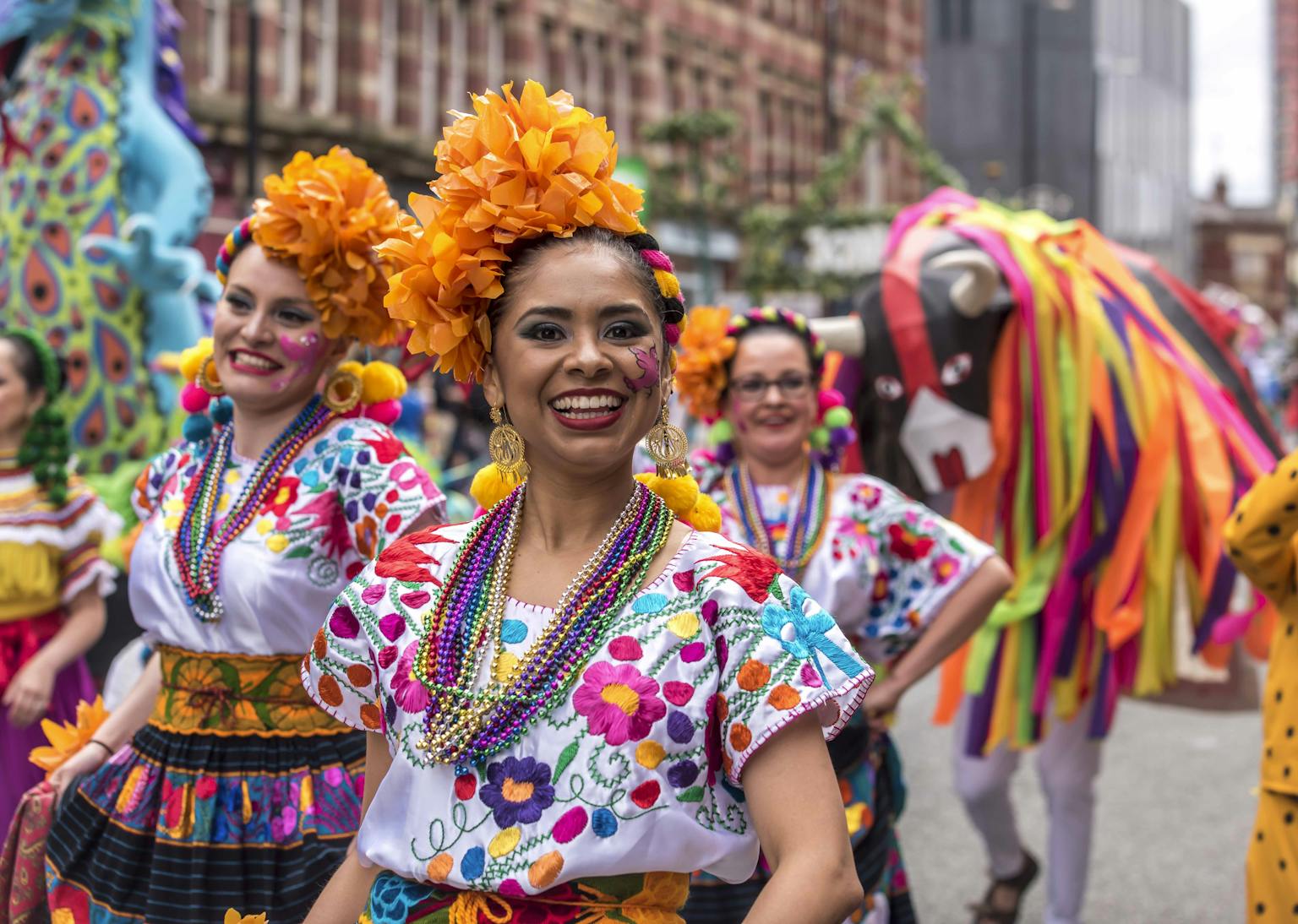 A group of Mexican dancers dressed up in colourful floral wear smiling. 