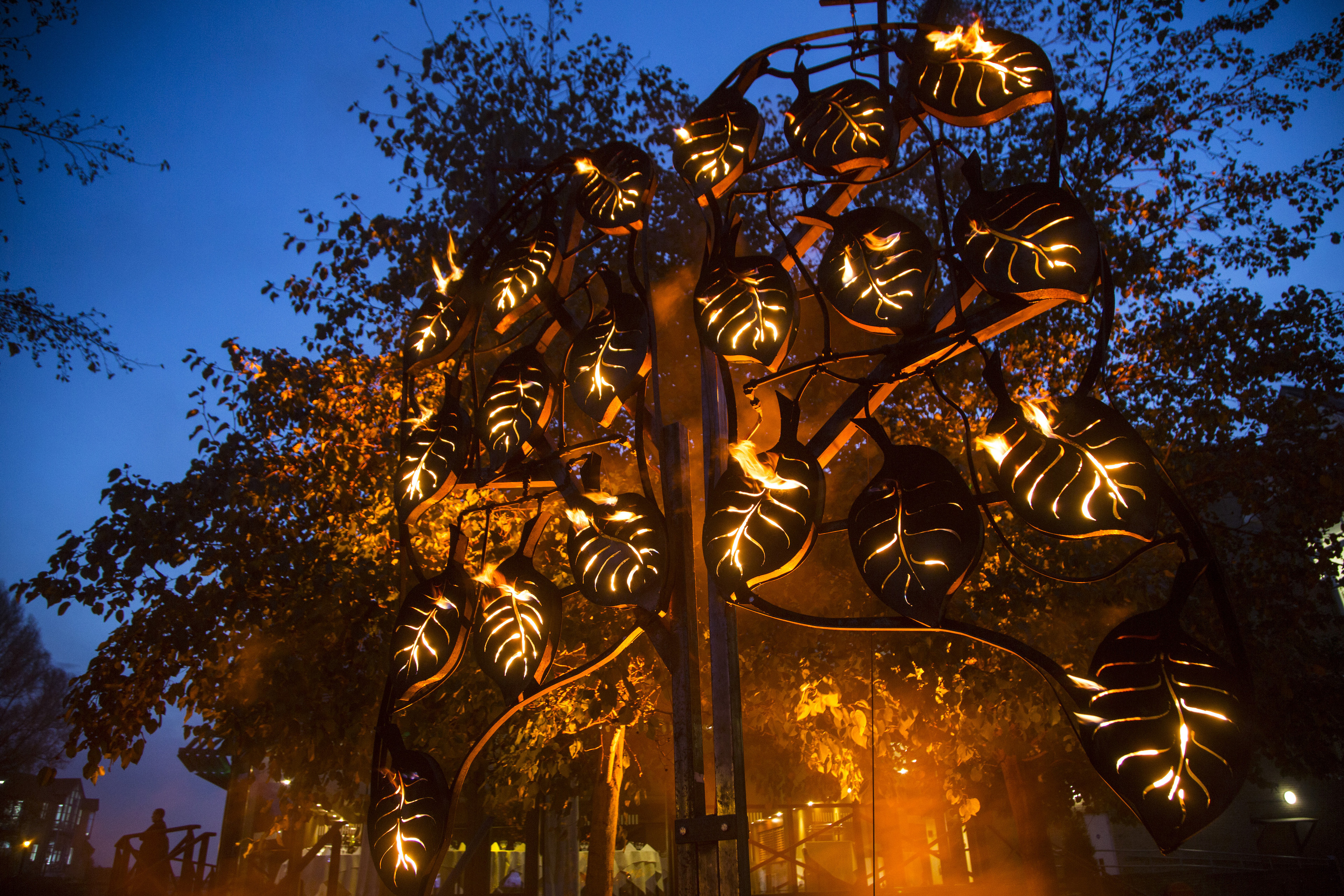 A blazing fire tree sculpture in a woodland area at dark.