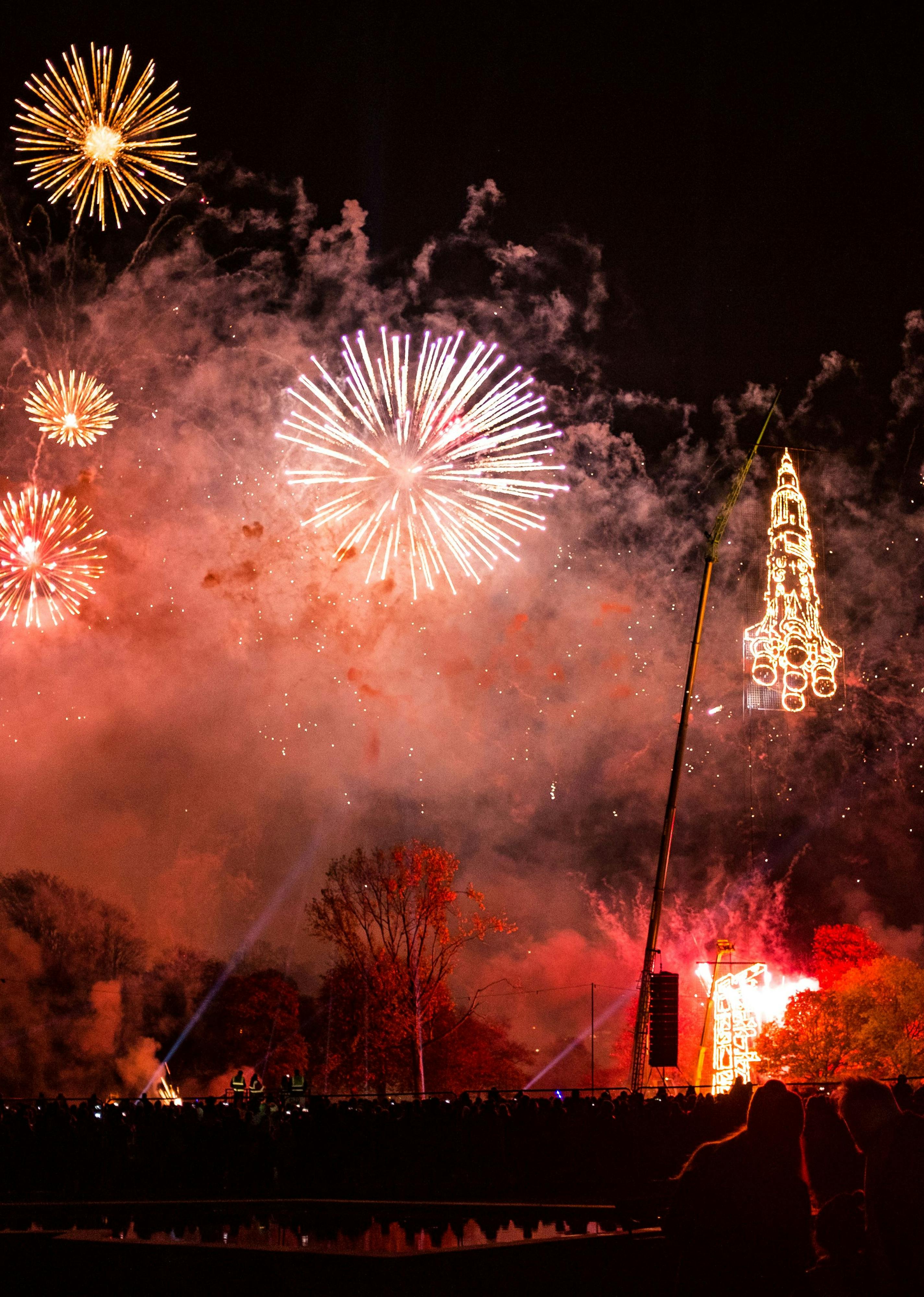 A night sky full of red fireworks and the lit-up image of a rocket