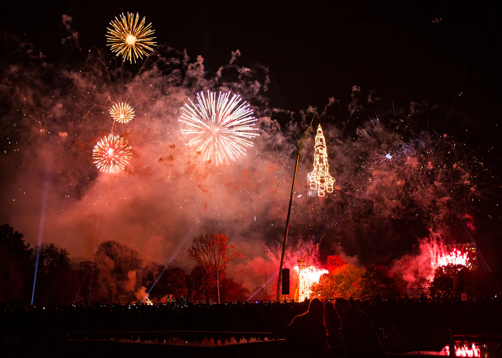 A night sky full of red fireworks and the lit-up image of a rocket