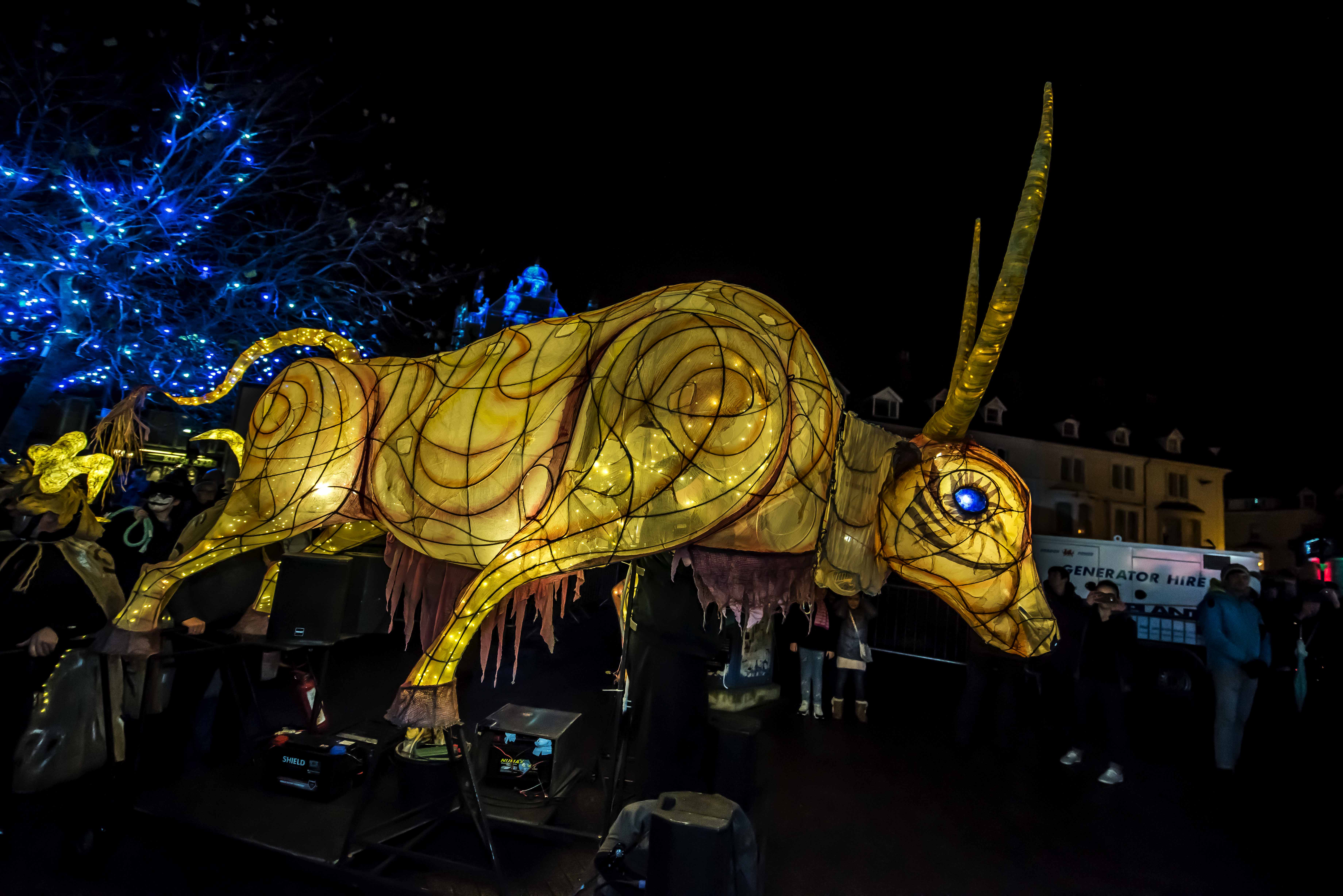 A large ox lit from within parading through a street