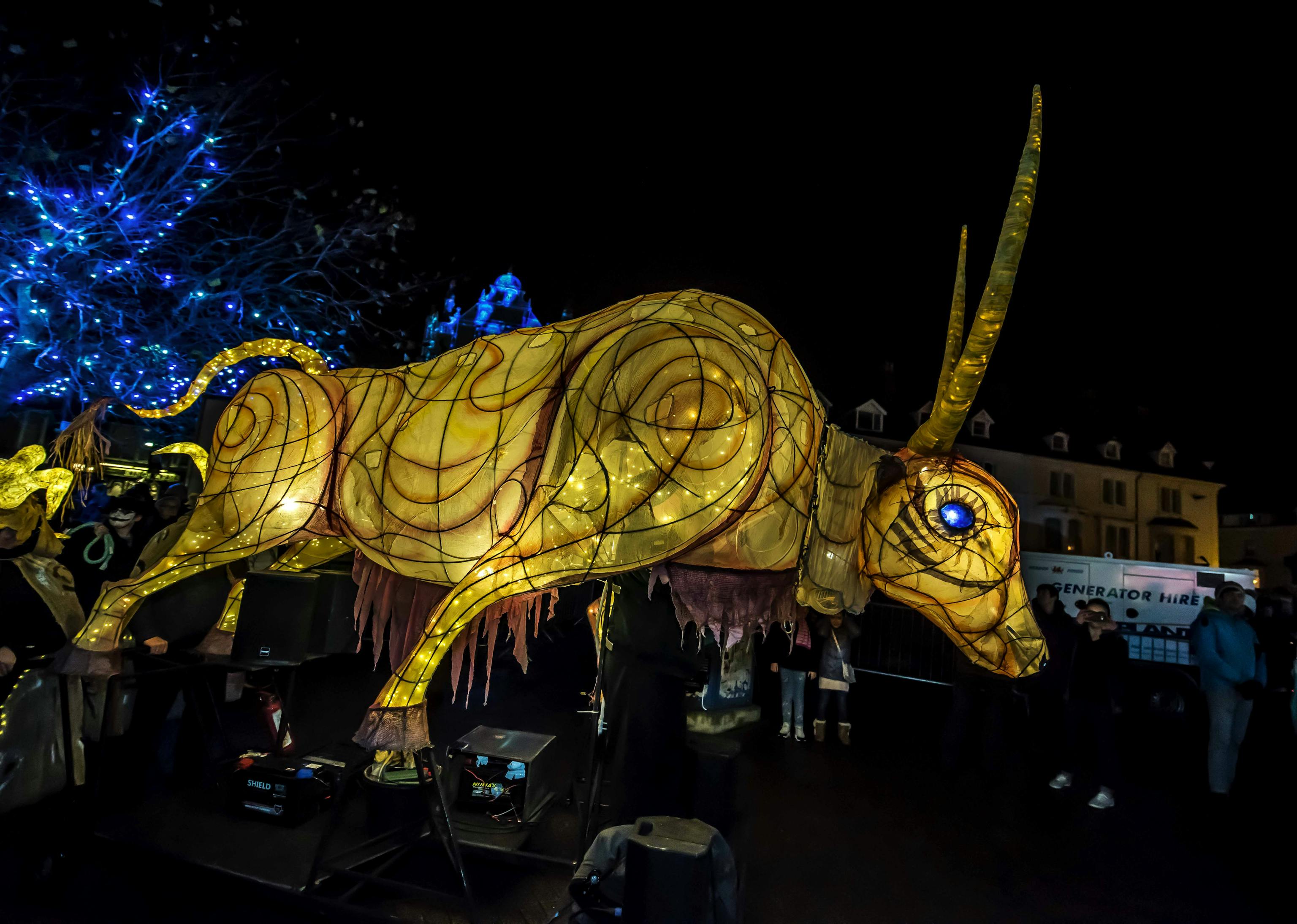 A large ox lit from within parading through a street