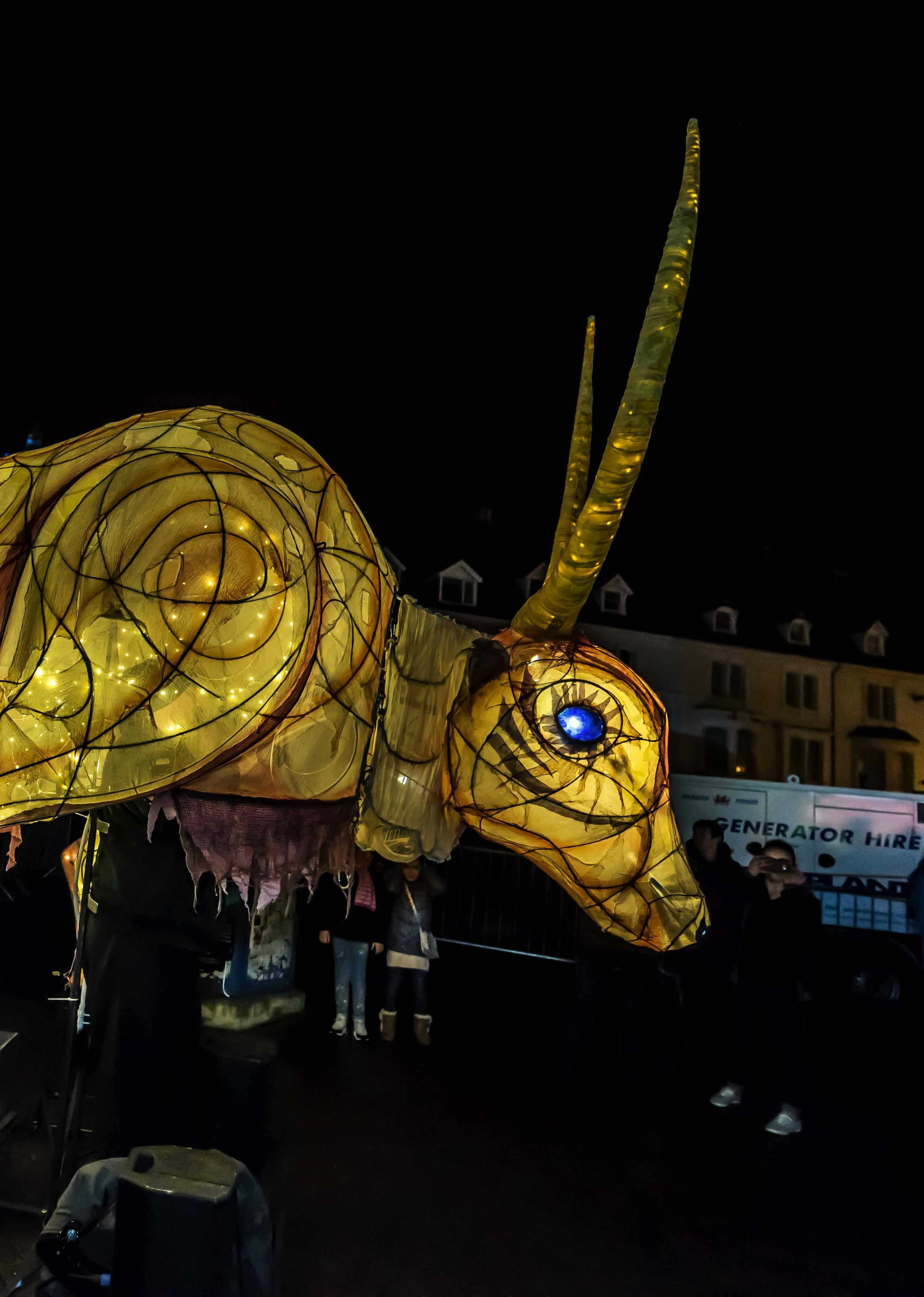 A large ox lit from within parading through a street
