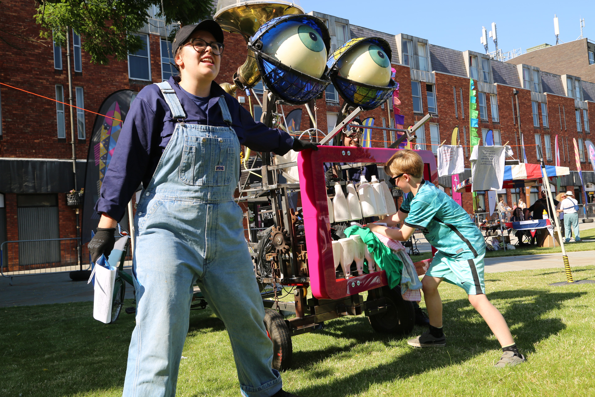 A giant face structure, with a wide mouth showing teeth, with blue eyes, being guided by a performer in dungarees.