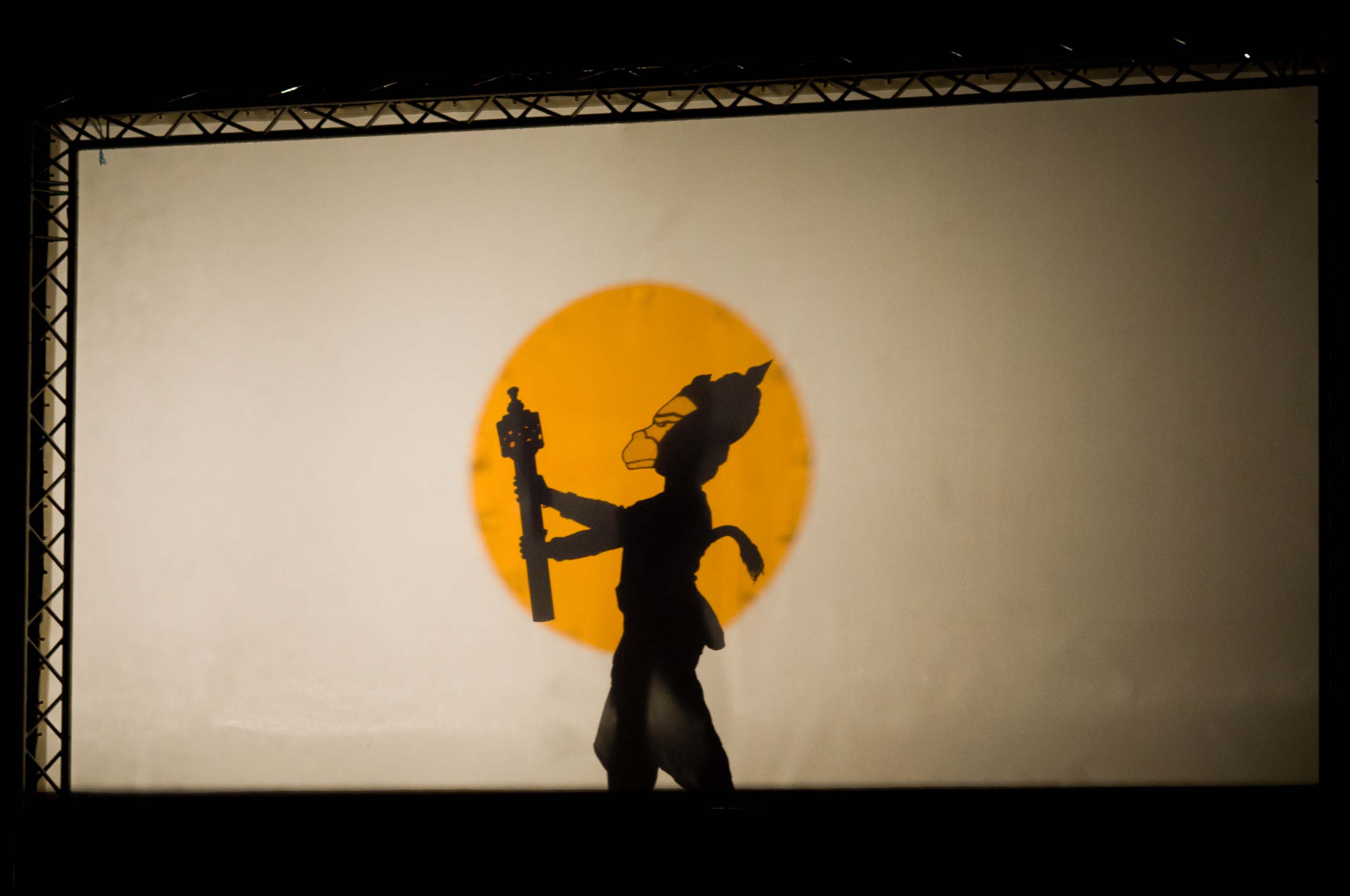 A shadow puppet of a monkey against a yellow circle