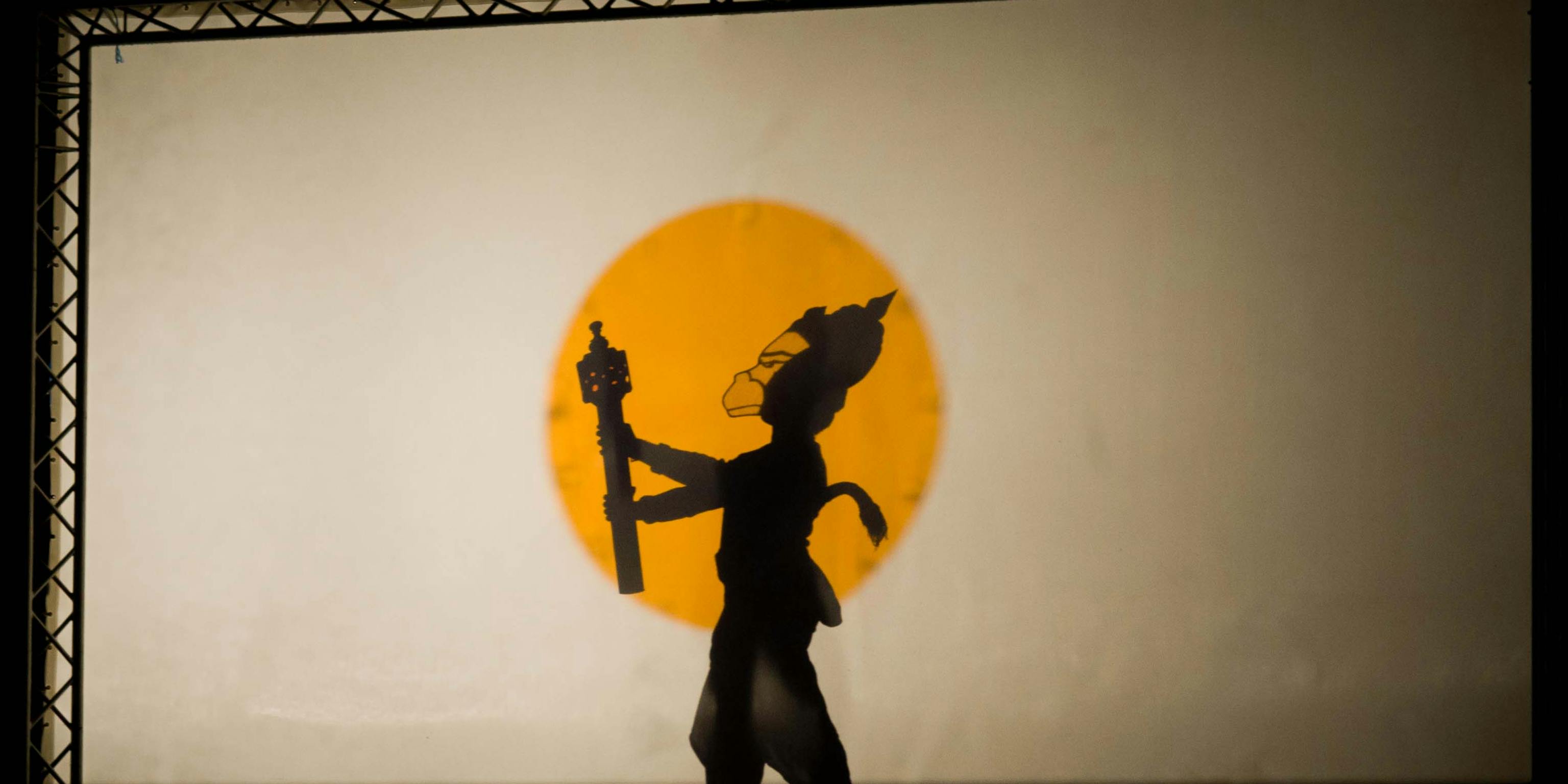 A shadow puppet of a monkey against a yellow circle