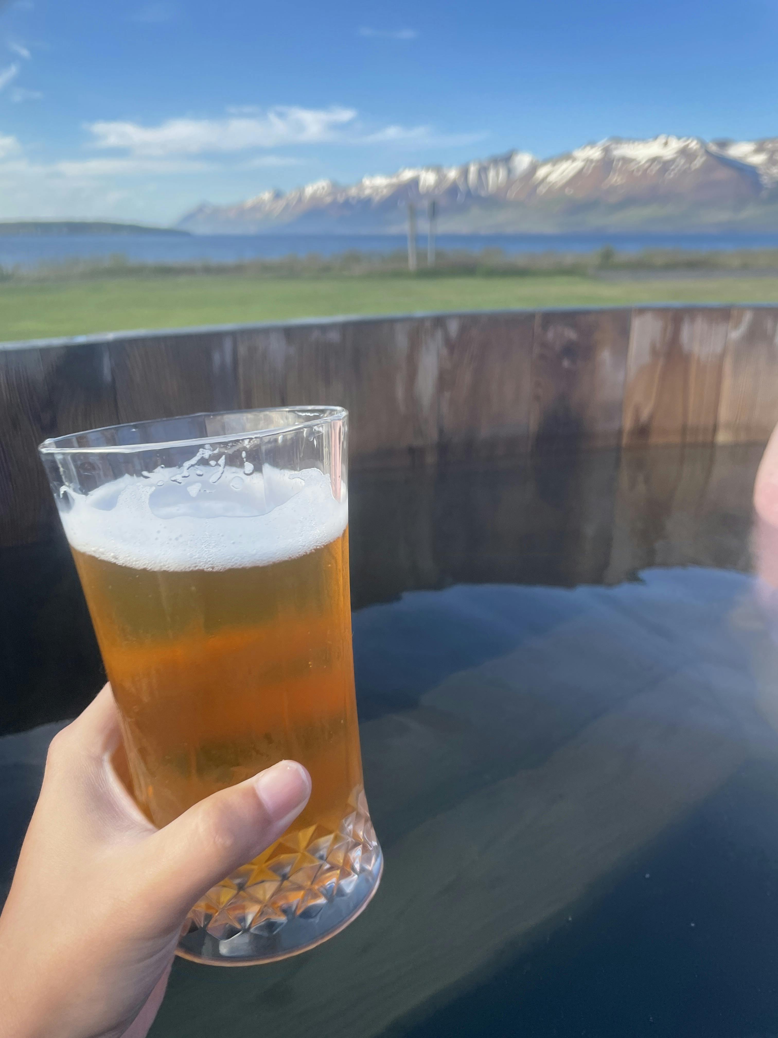 Hand holding beer in a hot tube with mountains in the distance