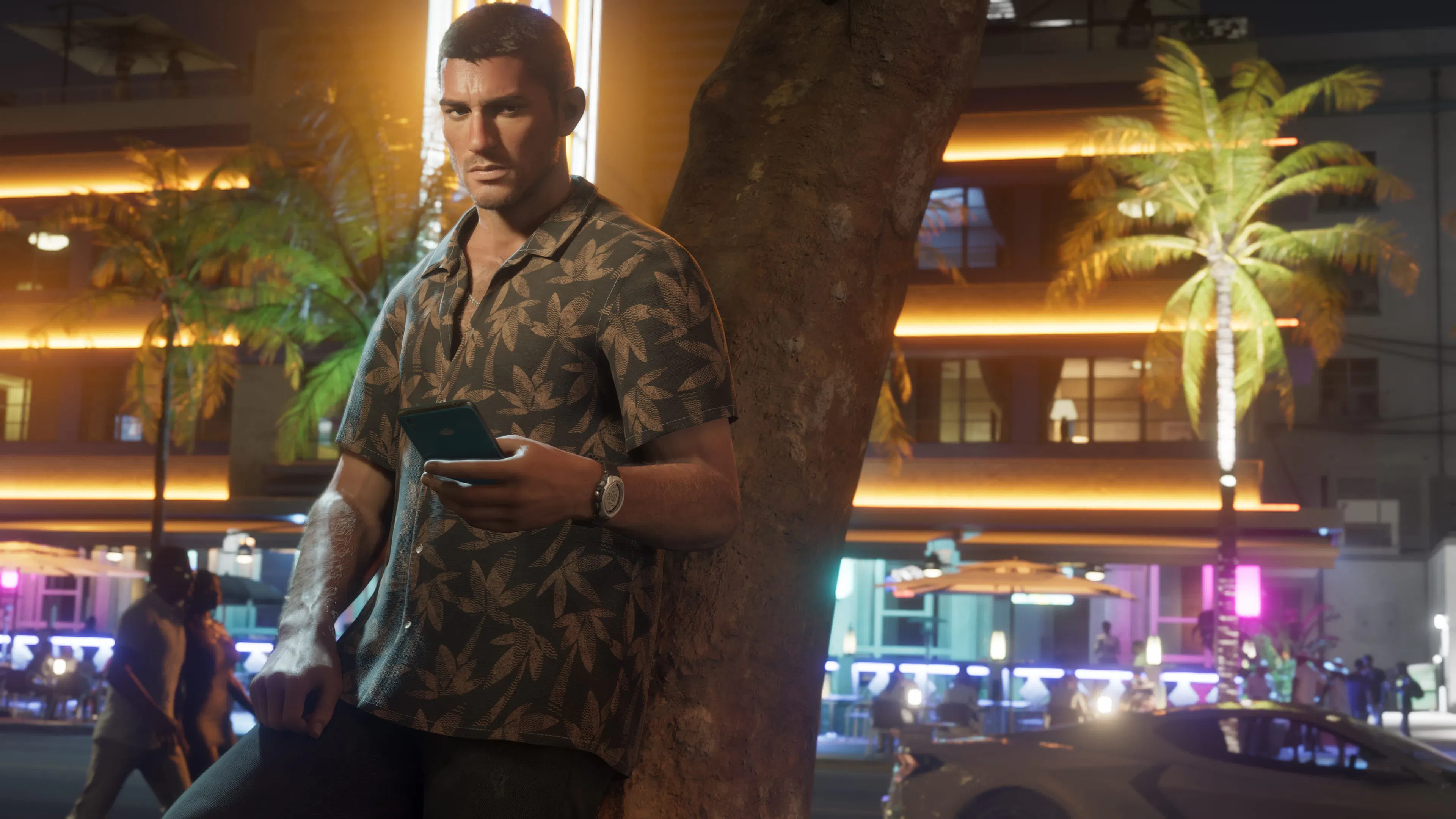 Jason consulte son téléphone sous un arbre, la nuit, devant des hôtels Art déco éclairés au néon.