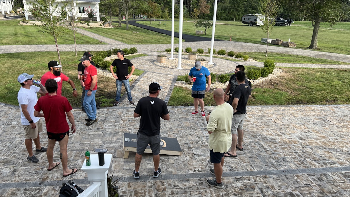 A group of 9 Marines from 1st Platoon CLR 15 stands around a cornhole board while talking and taking in the beauty of Patriot Point along with two staff members from WRF and Witness to War.