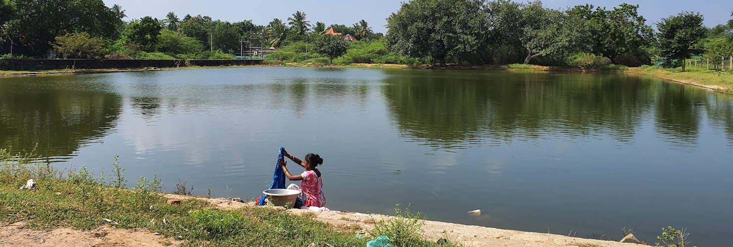 Woman handwashing clothes beside a shared water reservoir, 2018, South India