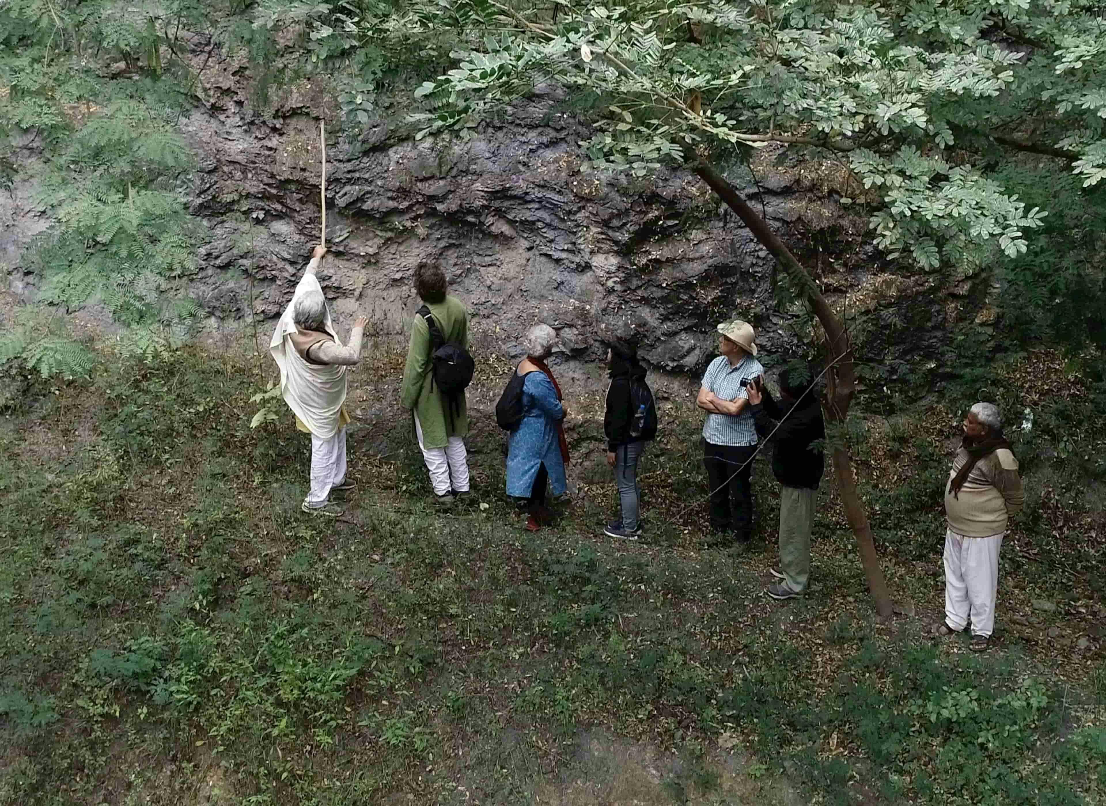 Rajendra Singh points to important features in the geology of a rock wall while Zach Weiss and others listen