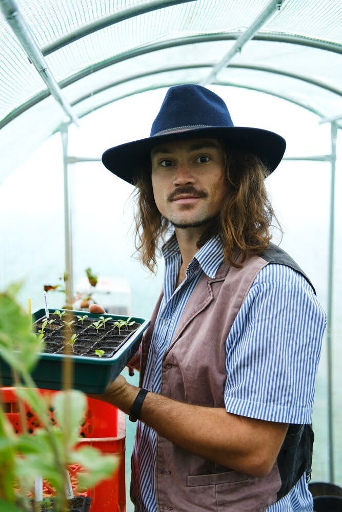 Nick Steiner holding a tray of seedling starts inside a greenhouse