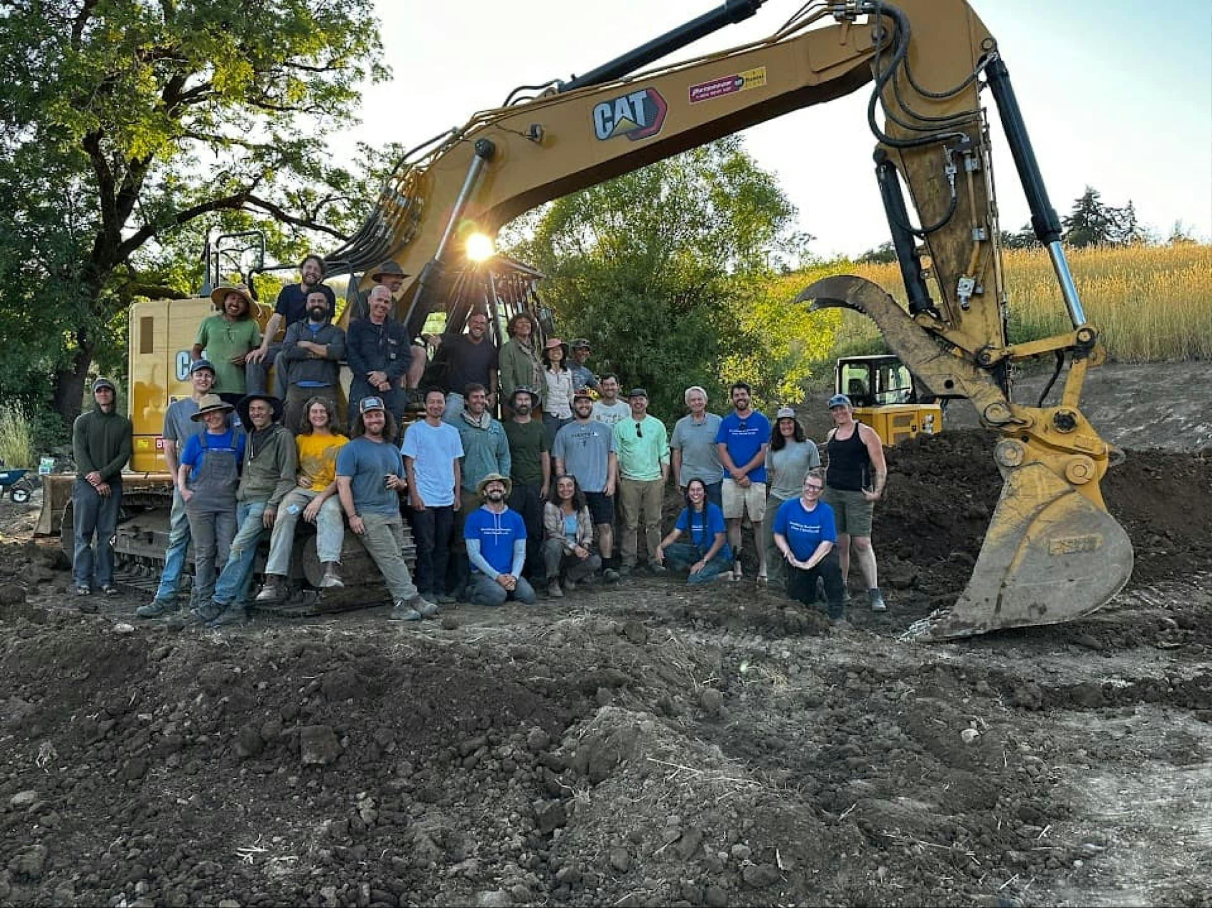 The Water Stories team and students group shot in front of an excavator at a project site during a workshop