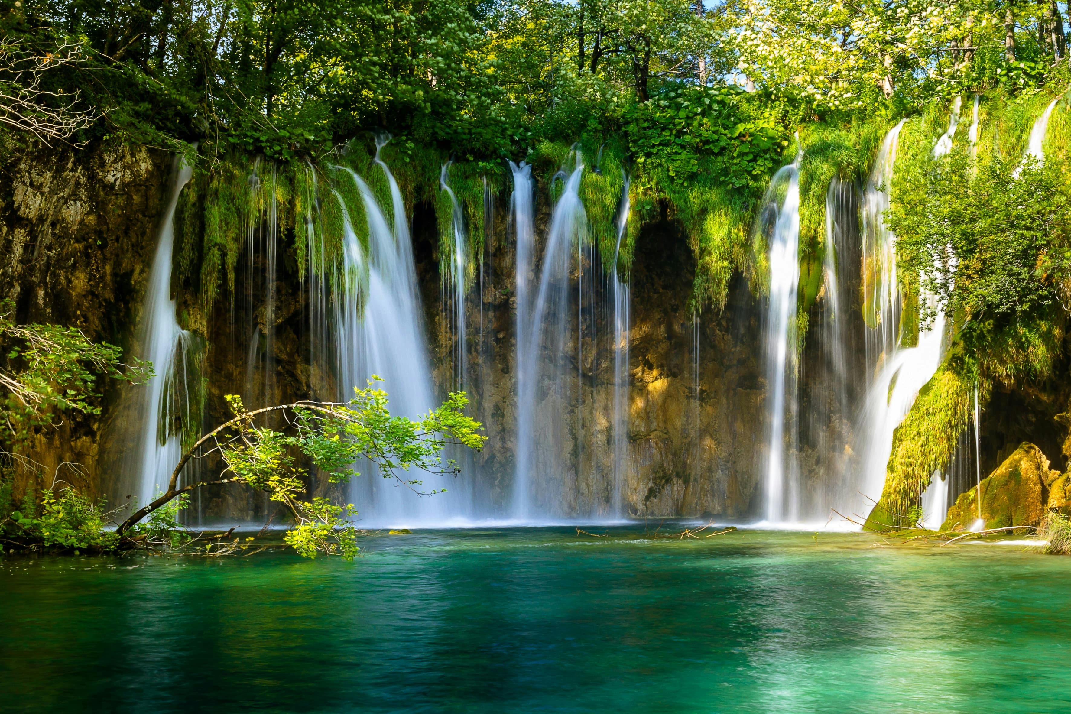 Water cascades in streams over rocks, forming a large waterfall in a lush oasis