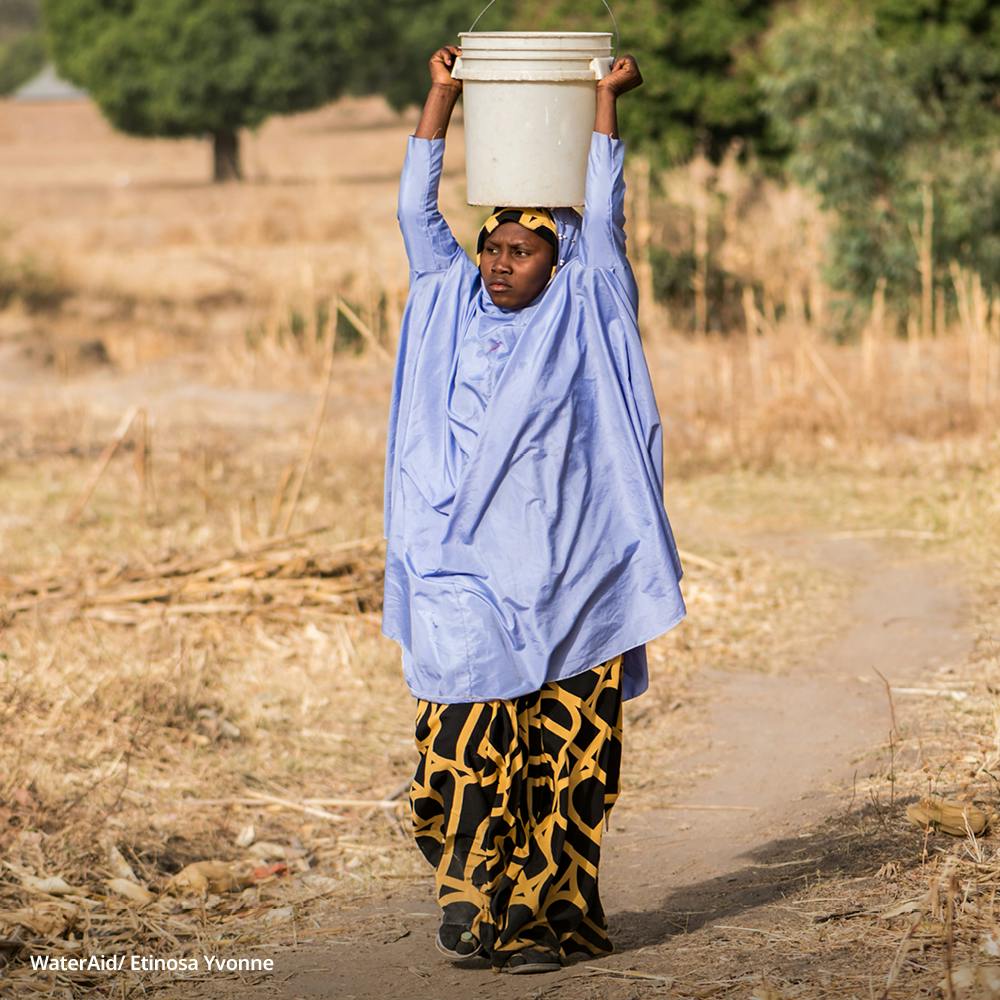 Karimatu carries a bucket of water on her head, Nigeria.