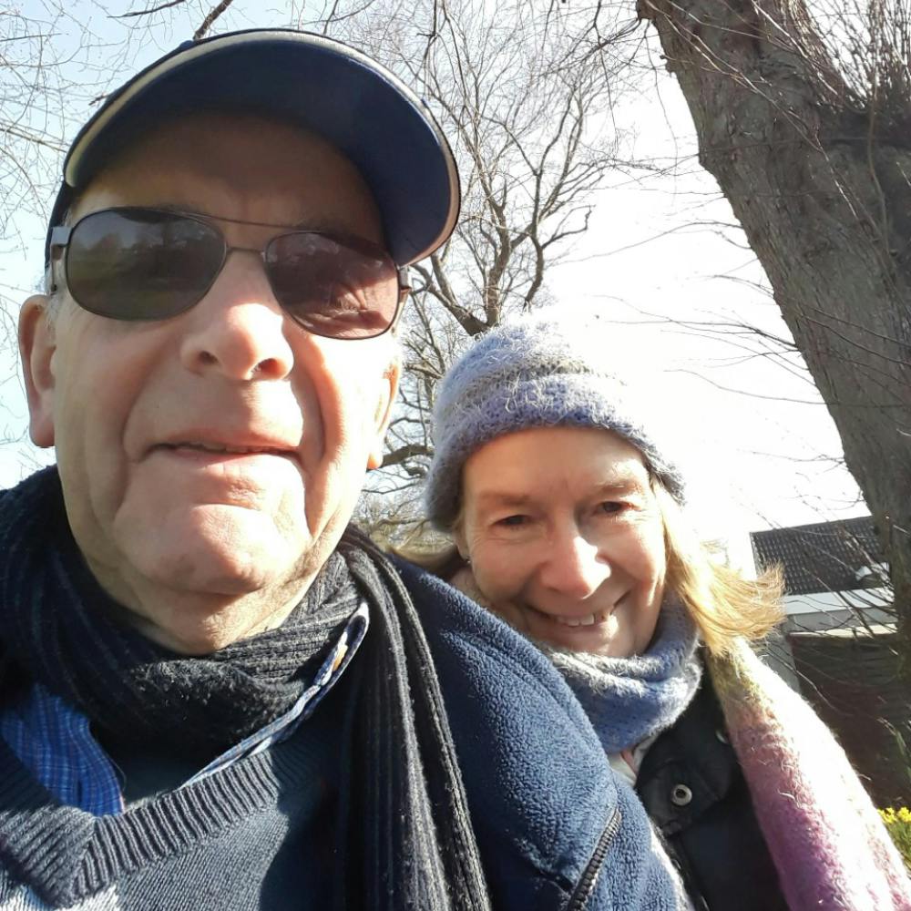 A man and a woman smiling on a walk next to some trees.
