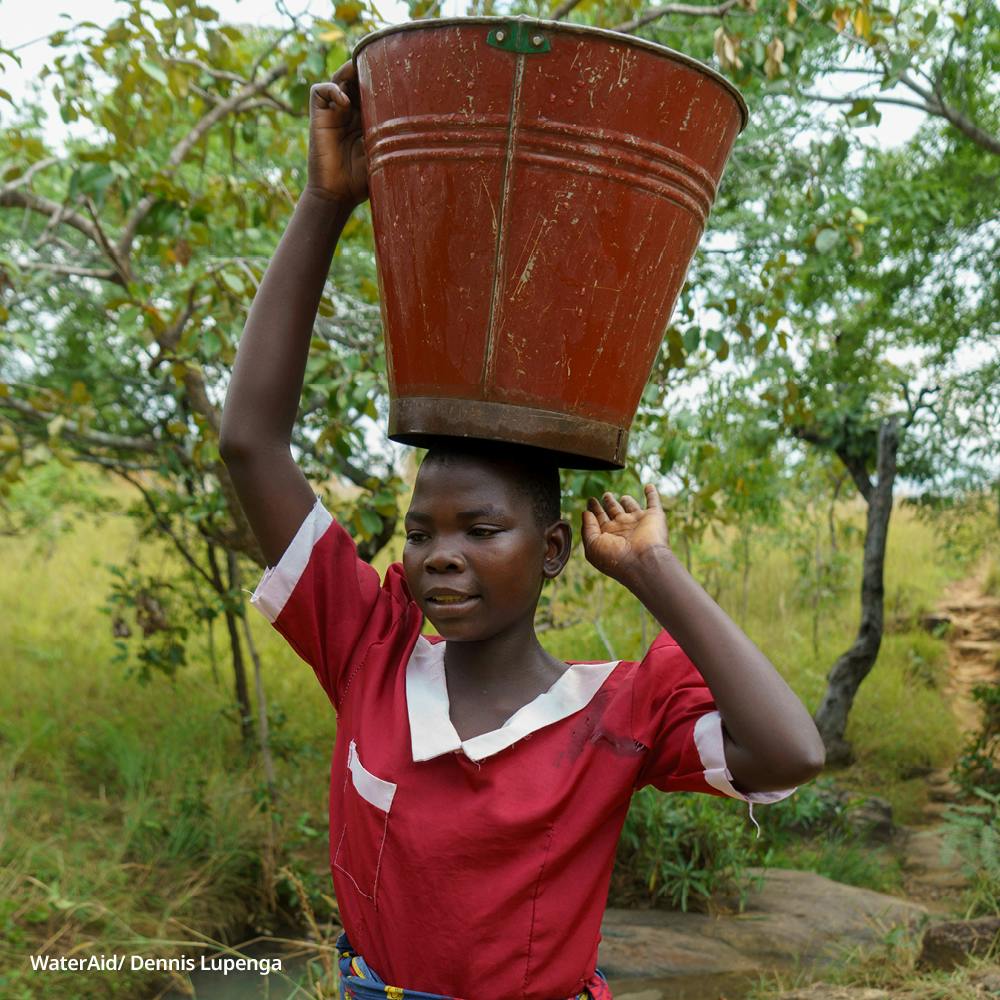 14-year-old Hawa carries a large bucket of water