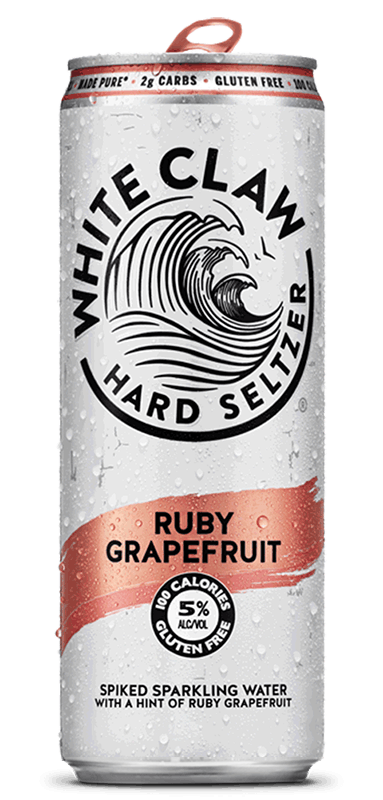 A can of White Claw® Hard Seltzer Ruby Grapefruit sits on rocks in front of the sea.