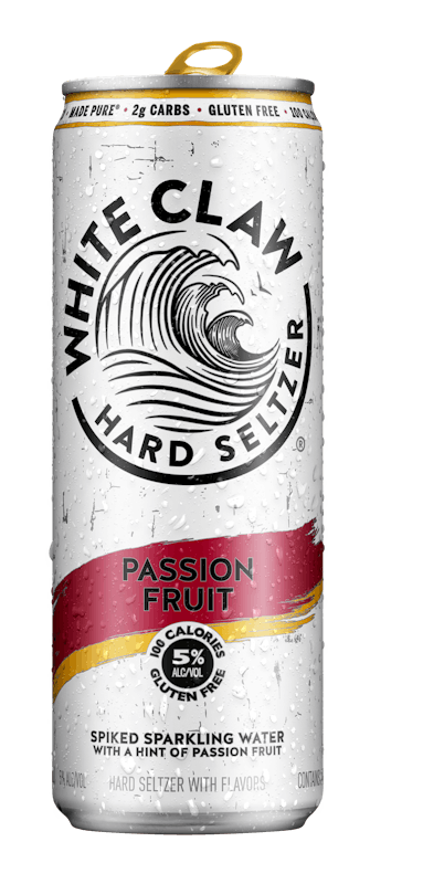 A can of White Claw® Hard Seltzer Passion Fruit sits on rocks in front of the sea. 