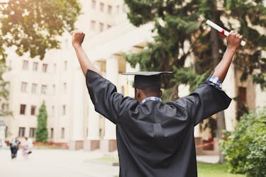 College graduate wearing a cap and gown holding his degree with his hands in the air