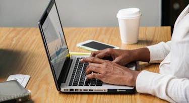 Person typing on a laptop during work with an iphone and coffee