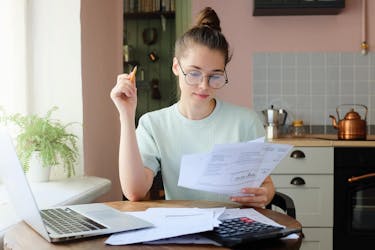 Female college student sitting in her kitchen looking at the cost of her student debt monthly payments