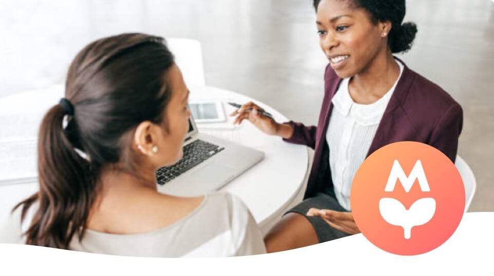 Two women sitting near a laptop, discussing something