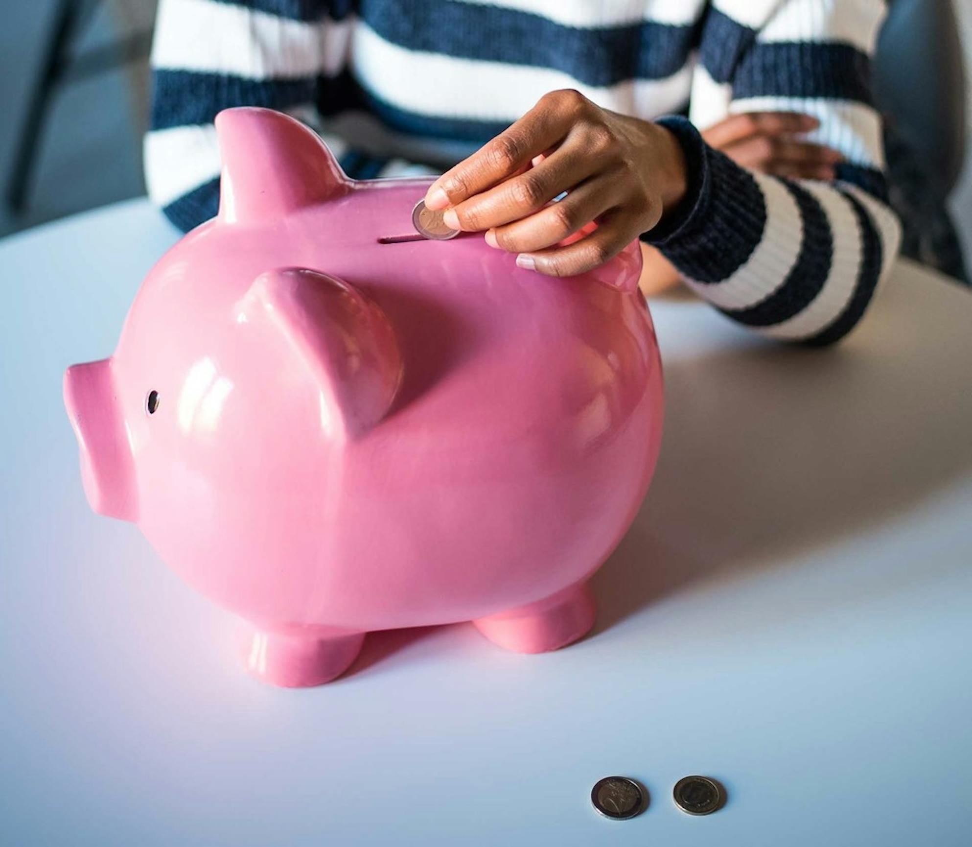 Woman sitting at a table saving money each month by putting coins into a piggy bank
