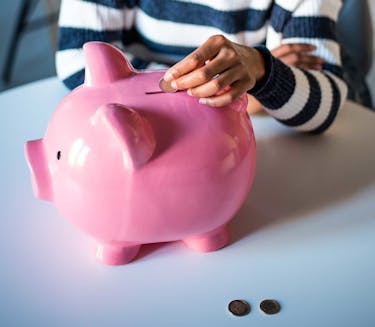 Woman sitting at a table saving money each month by putting coins into a piggy bank