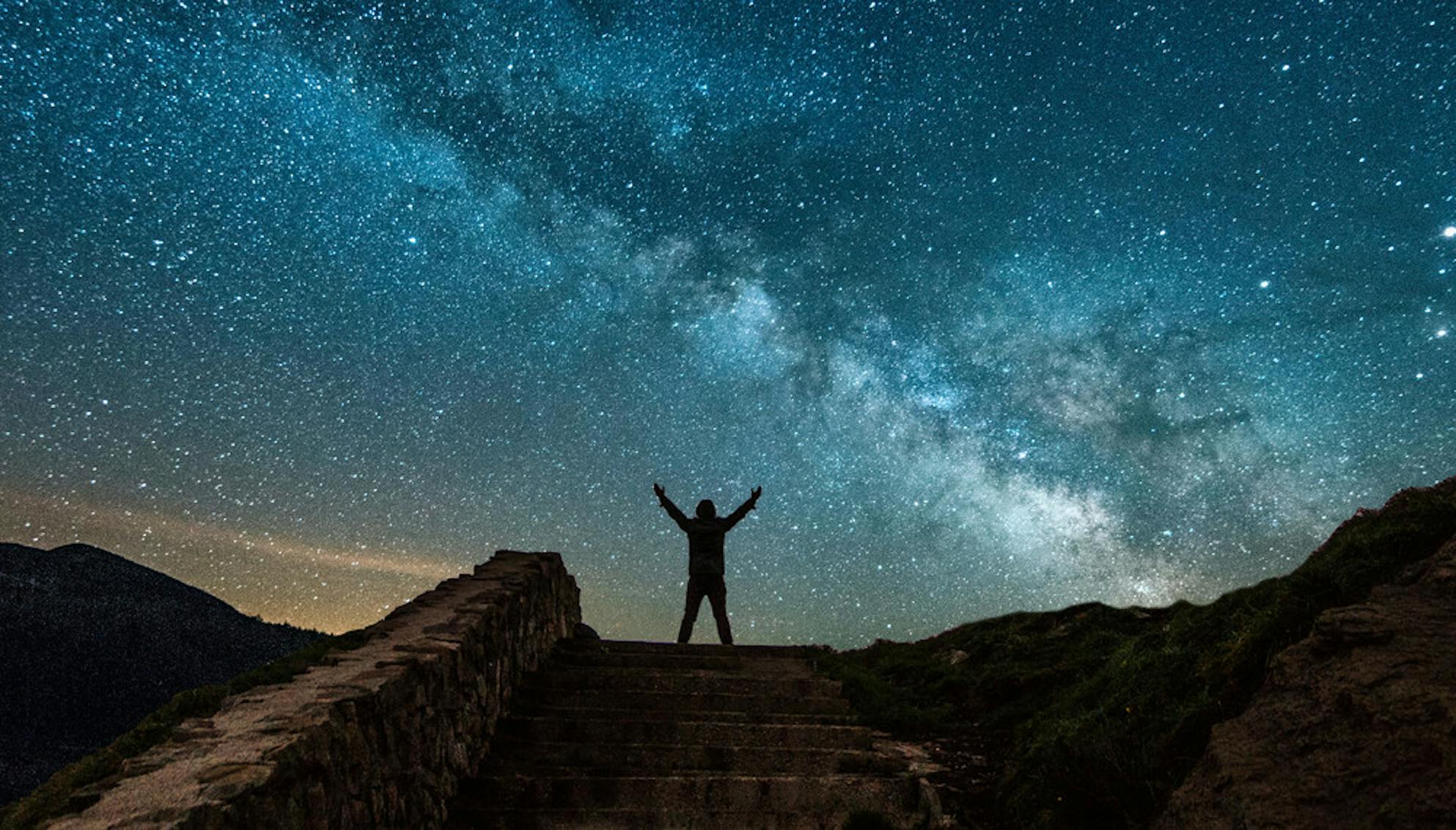 Man standing in the desert raising his hands towards the Milky Way galaxy