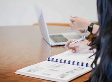 A married couple creating a plan for how to handle student debt using a note pad, a pen and a laptop