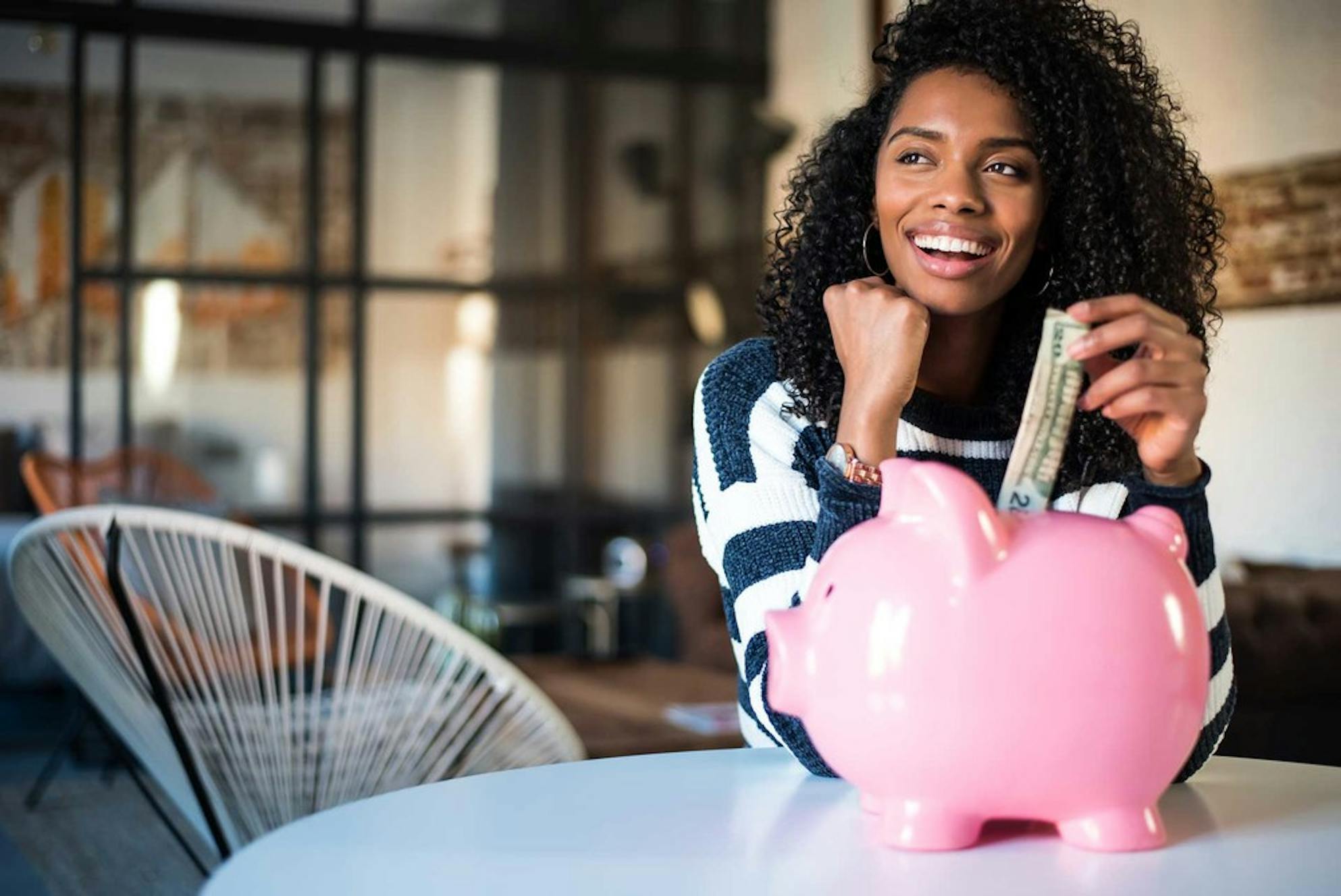 Woman saving money by putting cash in a pink piggy bank