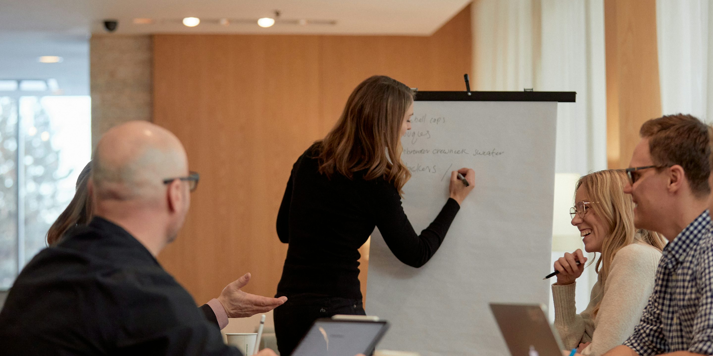 Shannon Hewlko writing on a large notepad while her team discusses corporate culture