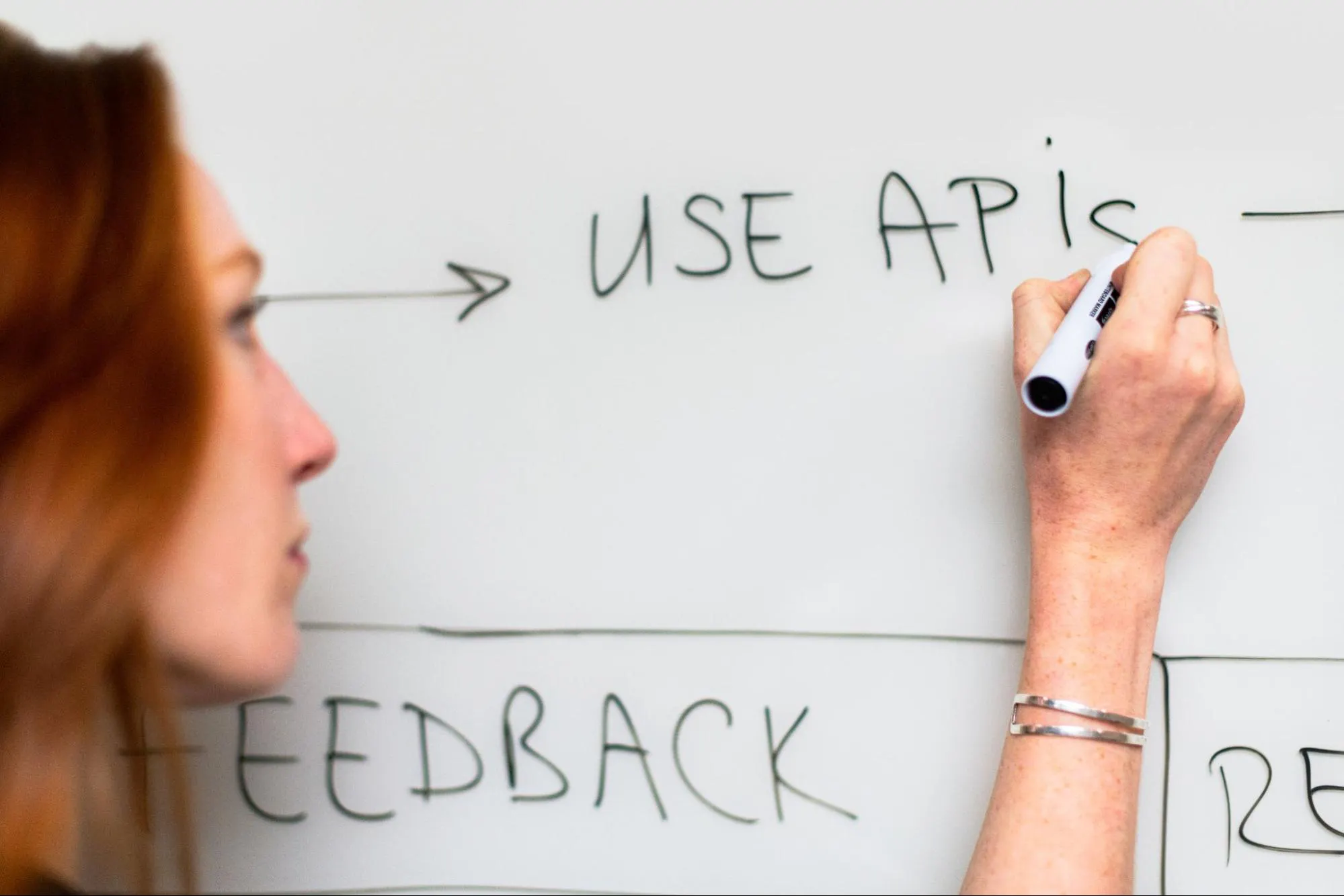 Close-up photo of someone writing USE APIs on a whiteboard with an arrow pointing to the text