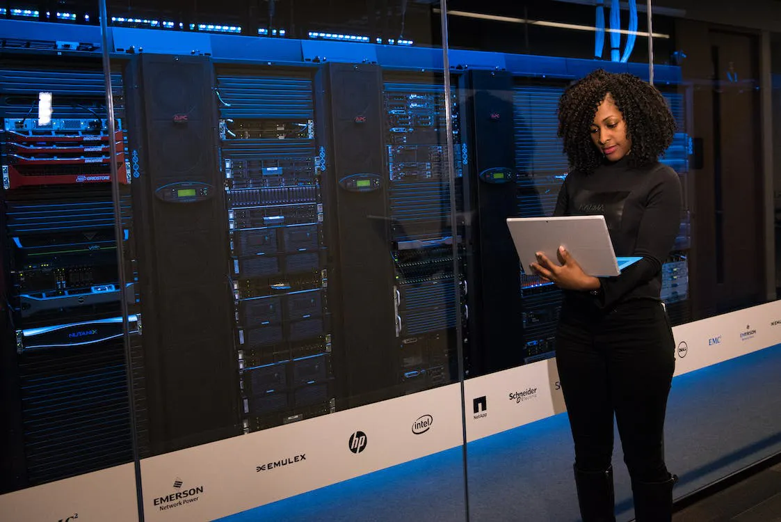 Photo of a person using a laptop in front of server racks in a data center