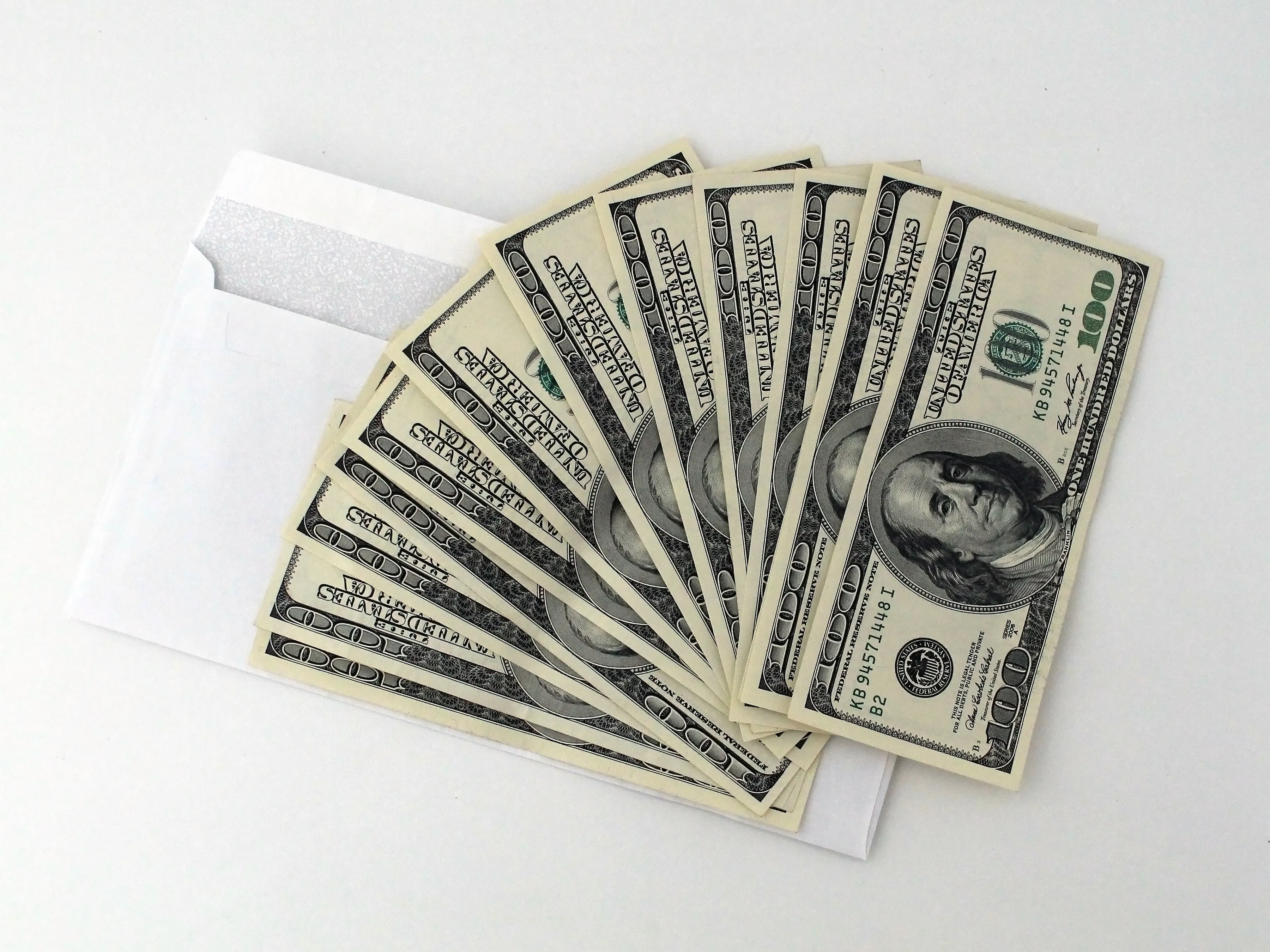 Photo of an envelope filled with US $100 bills fanned out on a white background