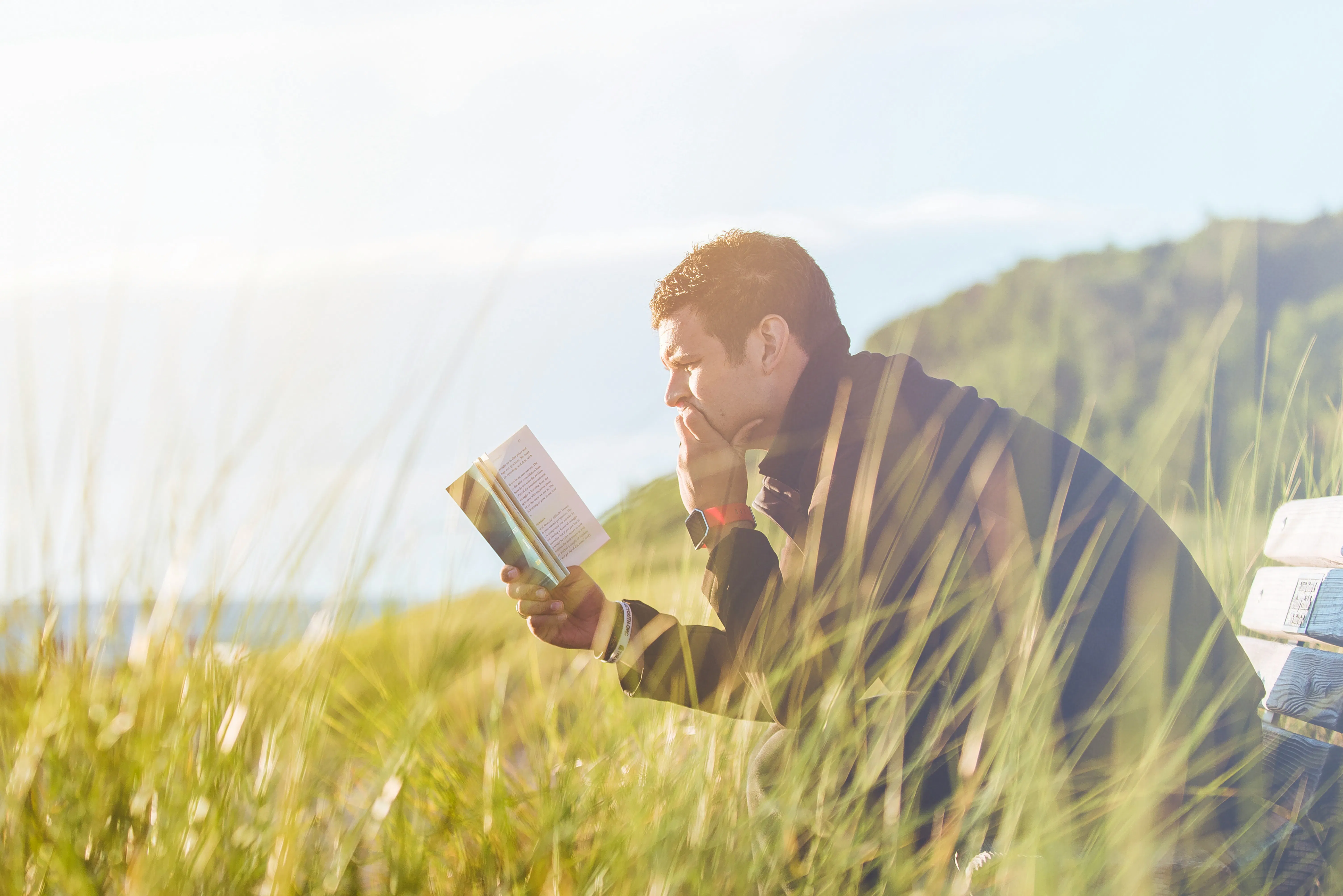 رجل يقرأ كتابًا على الشاطئ بالقرب من بحيرة خلال النهار
