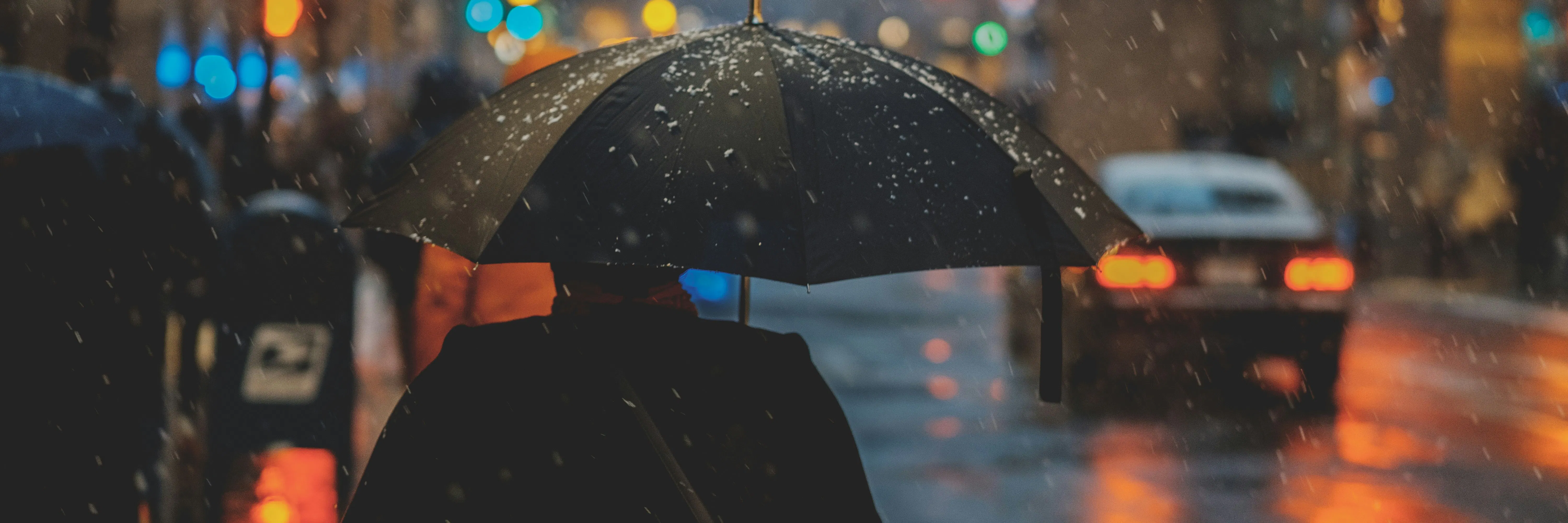 雨の中、傘を持って歩いている人と近くの車