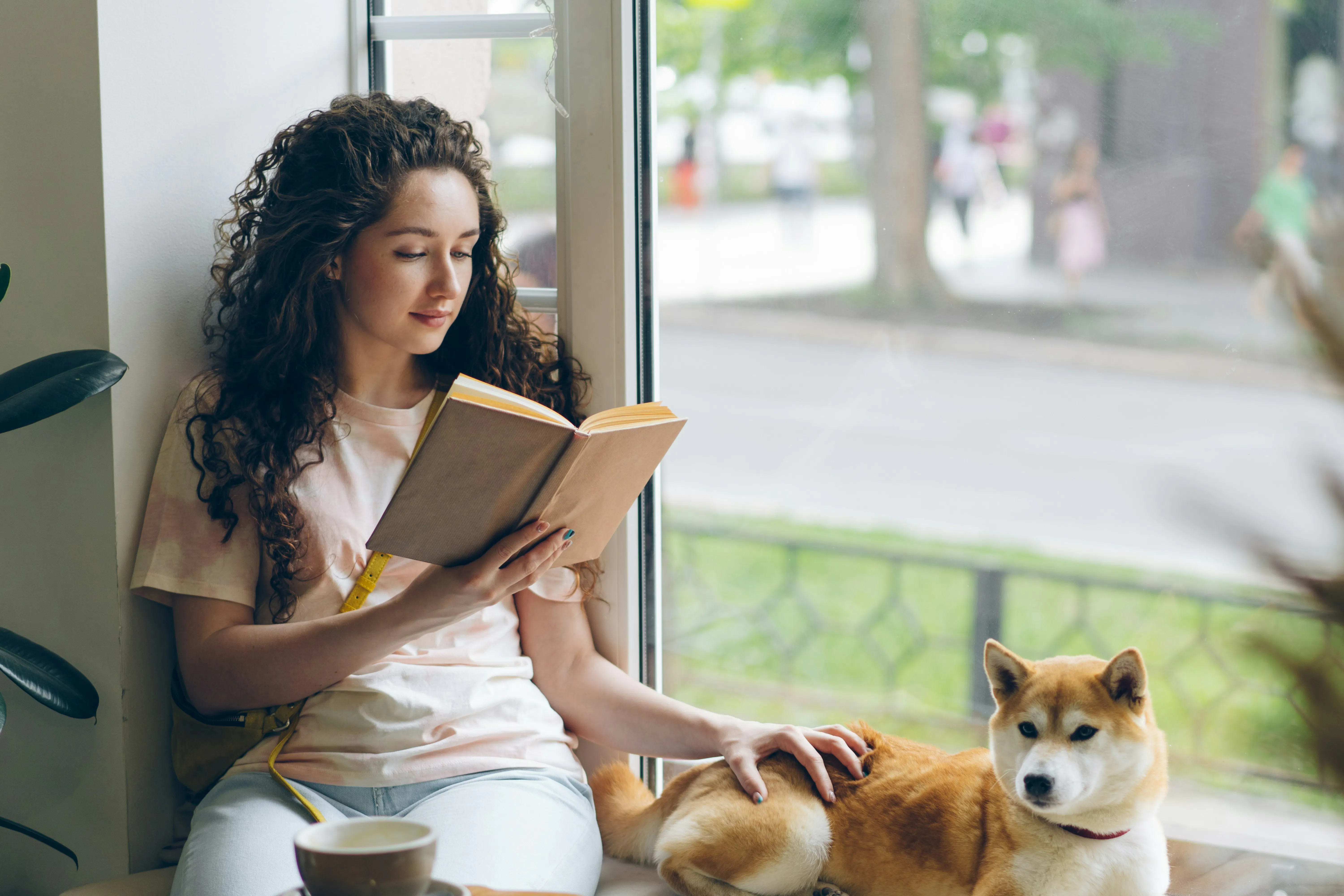 una donna seduta su un davanzale che legge un libro accanto a un cane