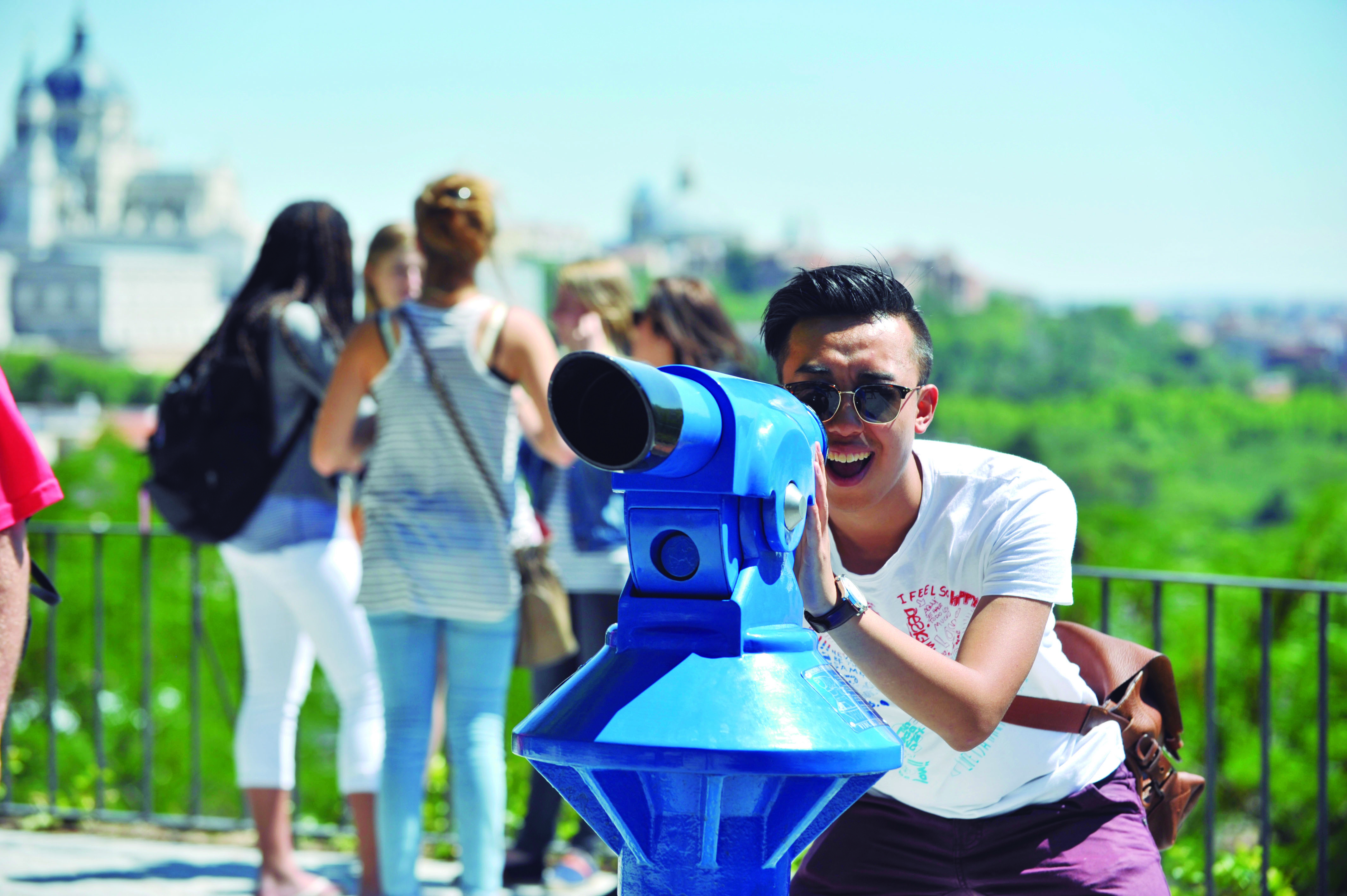 Jovem olhando através de um telescópio em um mirante em Madrid, Espanha, representando uma atividade de passeio turístico e vistas panorâmicas da cidade