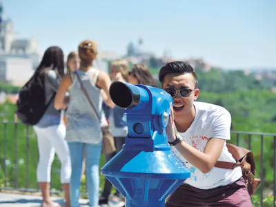 Jovem olhando através de um telescópio em um mirante em Madrid, Espanha, representando uma atividade de passeio turístico e vistas panorâmicas da cidade