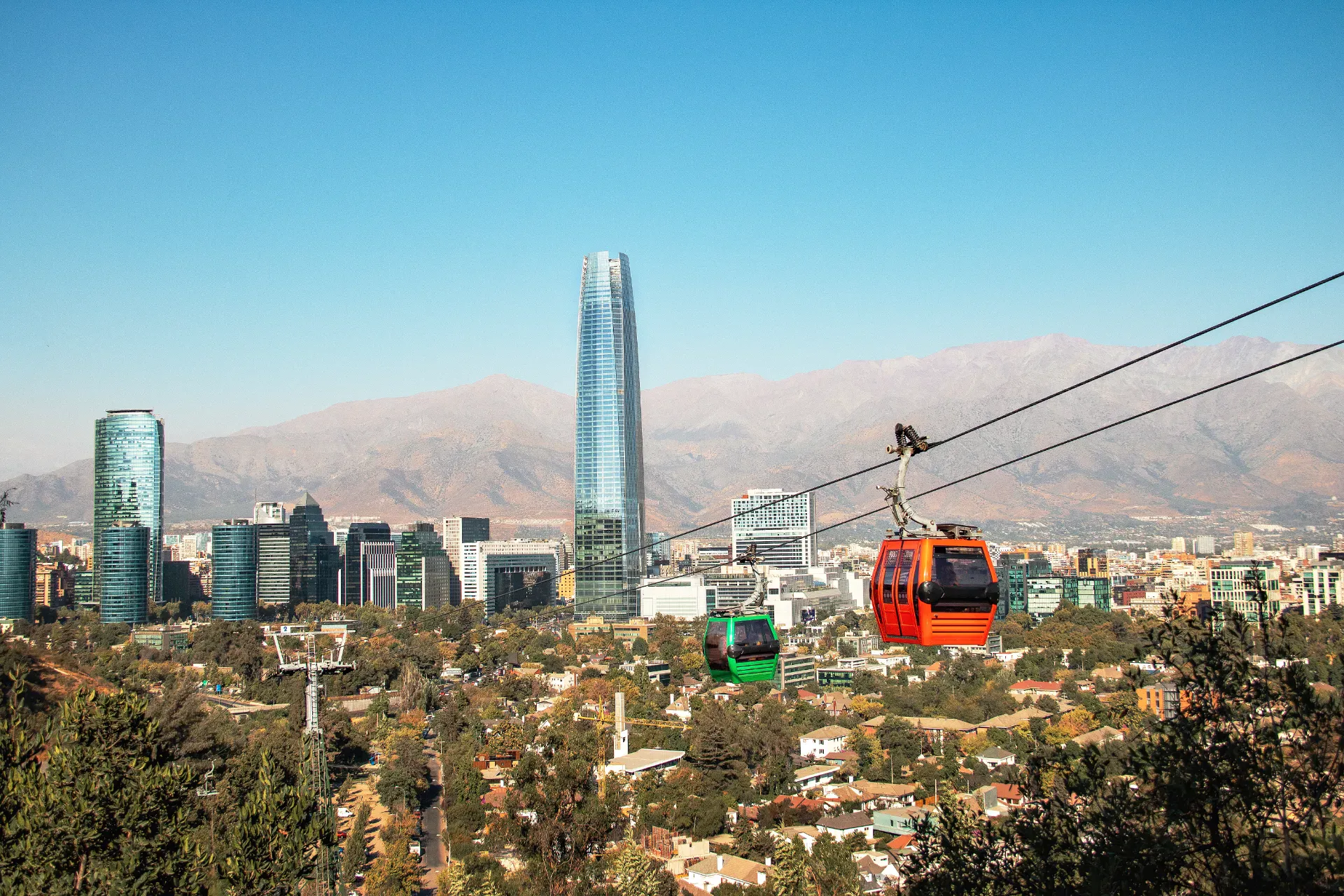 Cable cars above a modern city with skyscrapers and mountains in the background