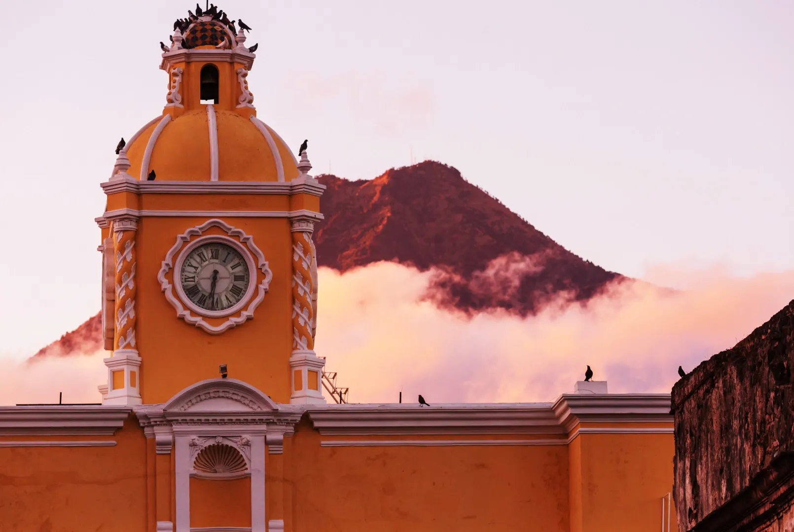 Torre dell'orologio coloniale in Guatemala con un vulcano sullo sfondo al tramonto