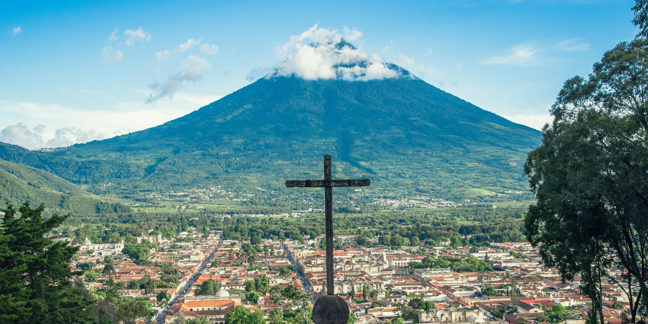 Vista di una città guatemalteca con una croce e un vulcano sullo sfondo sotto un cielo sereno