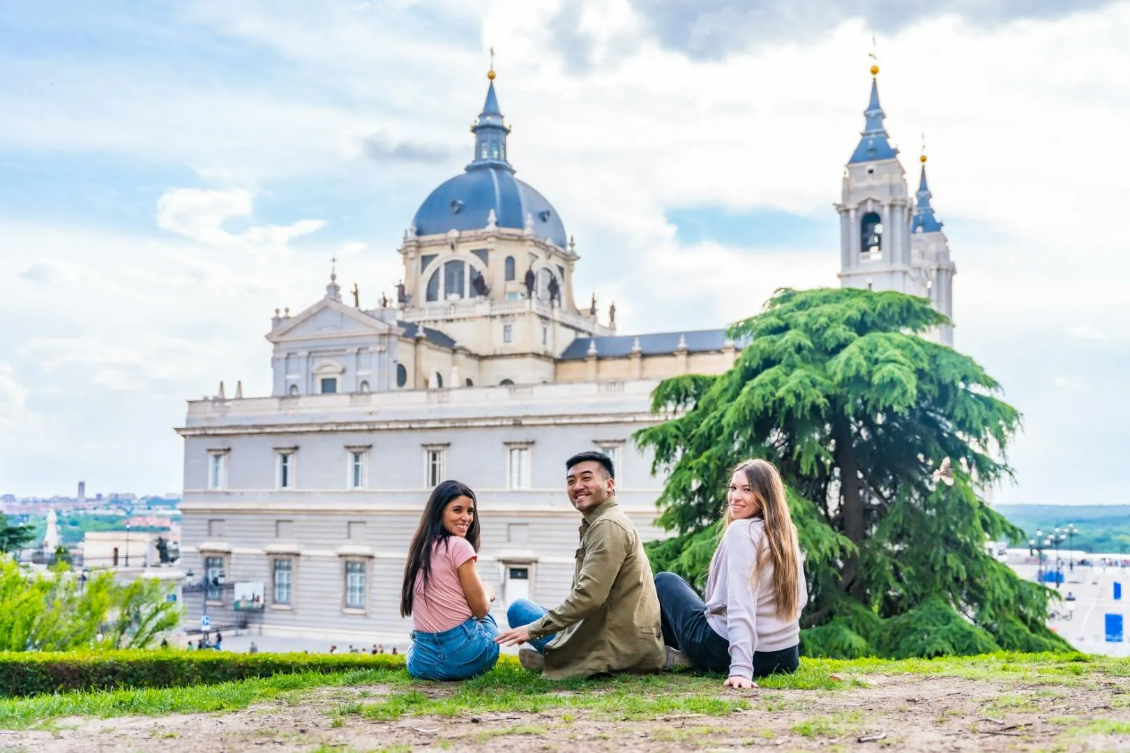 Tre studenti seduti davanti al Palazzo Reale di Madrid, mentre si godono la vista della città.