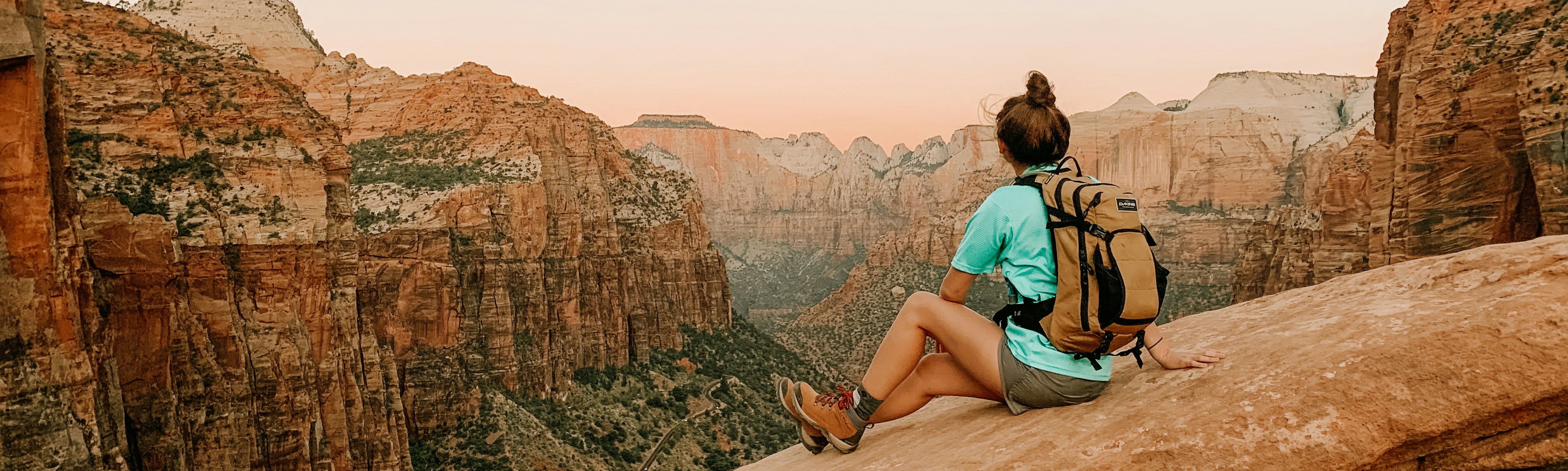 woman in teal tank top sitting on brown rock formation during daytime
