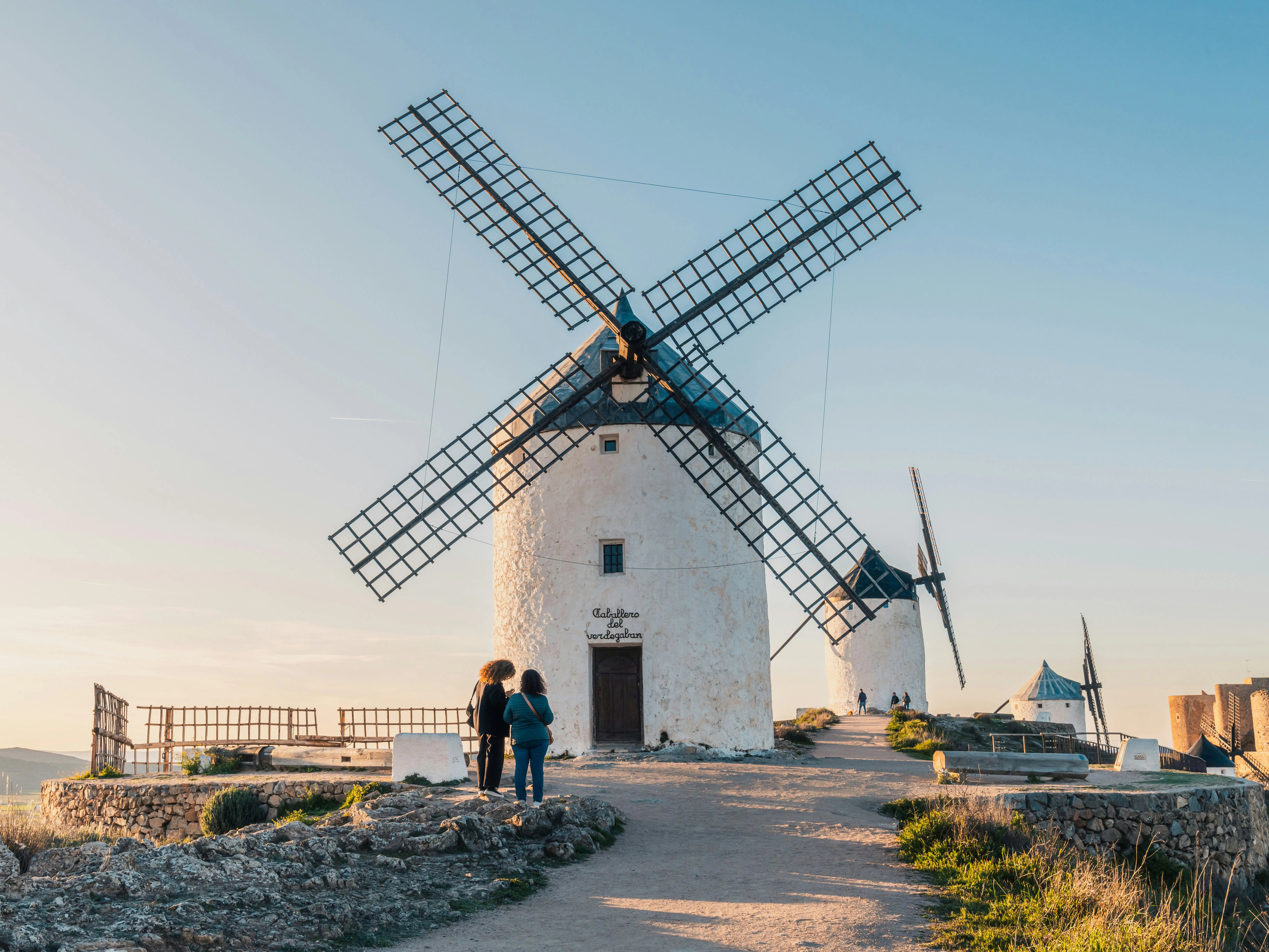 Two people stand before historic windmills at sunset.