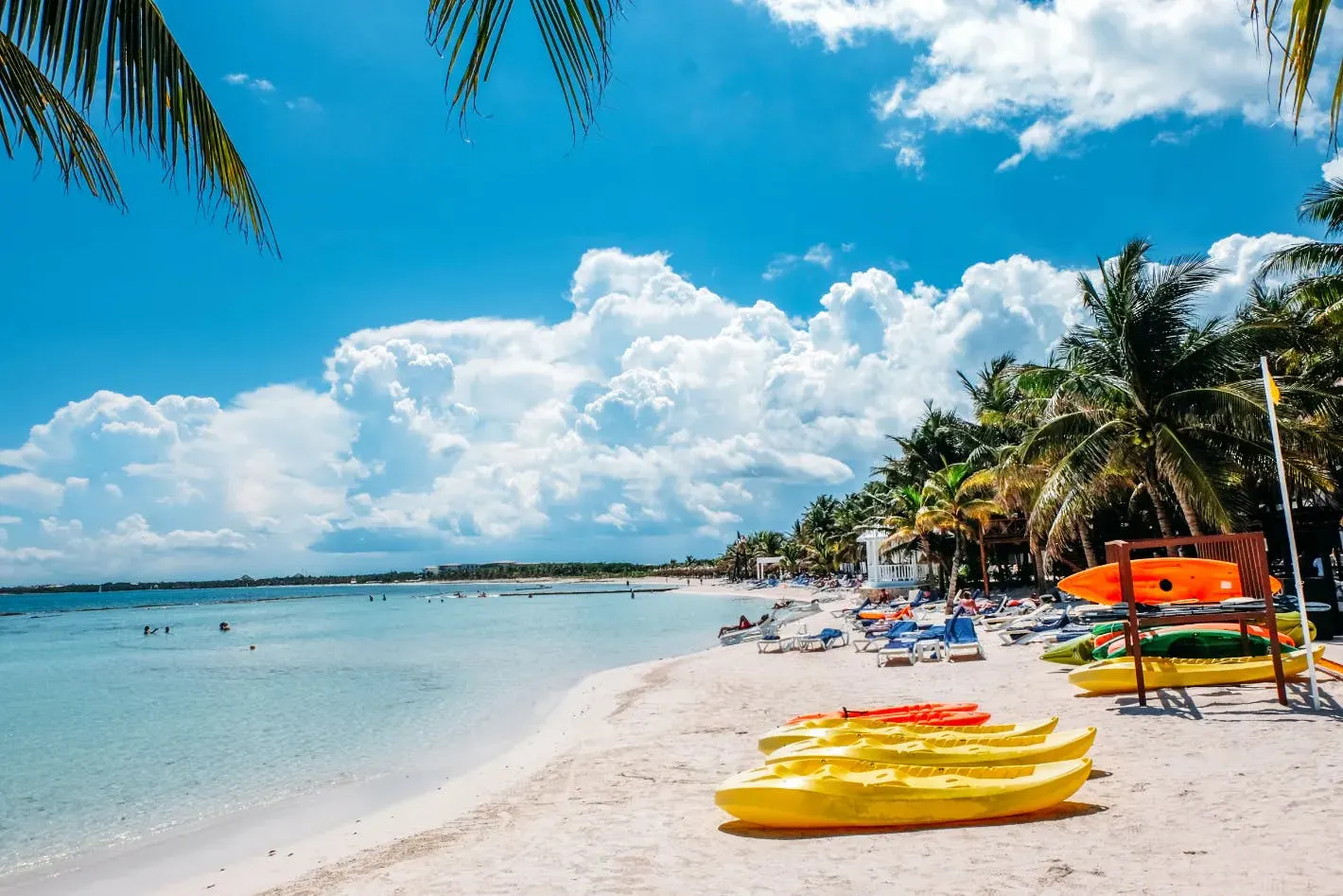 Spiaggia tropicale con kayak sulla sabbia, palme e acque calme sotto un cielo soleggiato