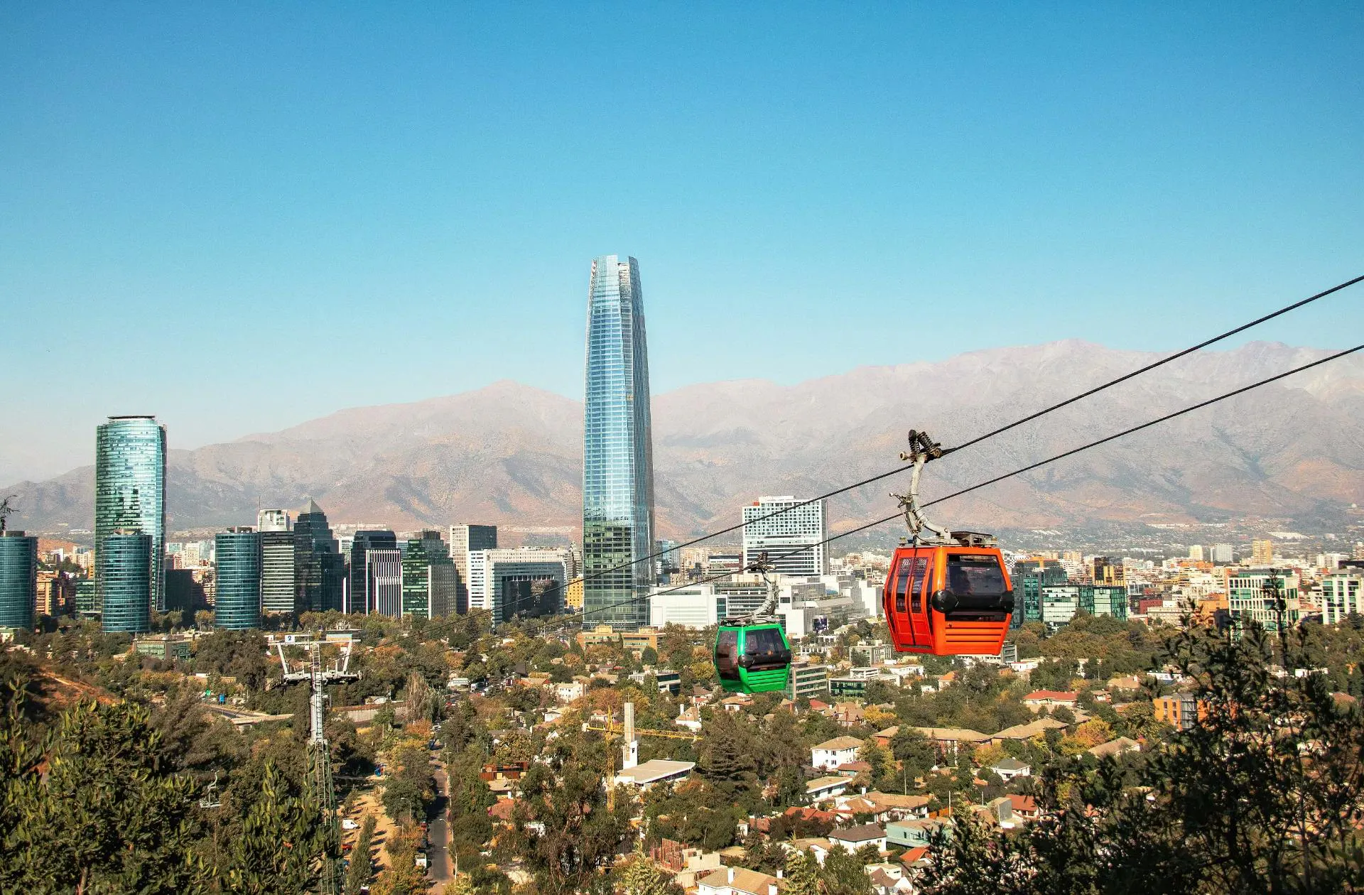 Funivie sopra una città moderna con grattacieli e montagne sullo sfondo