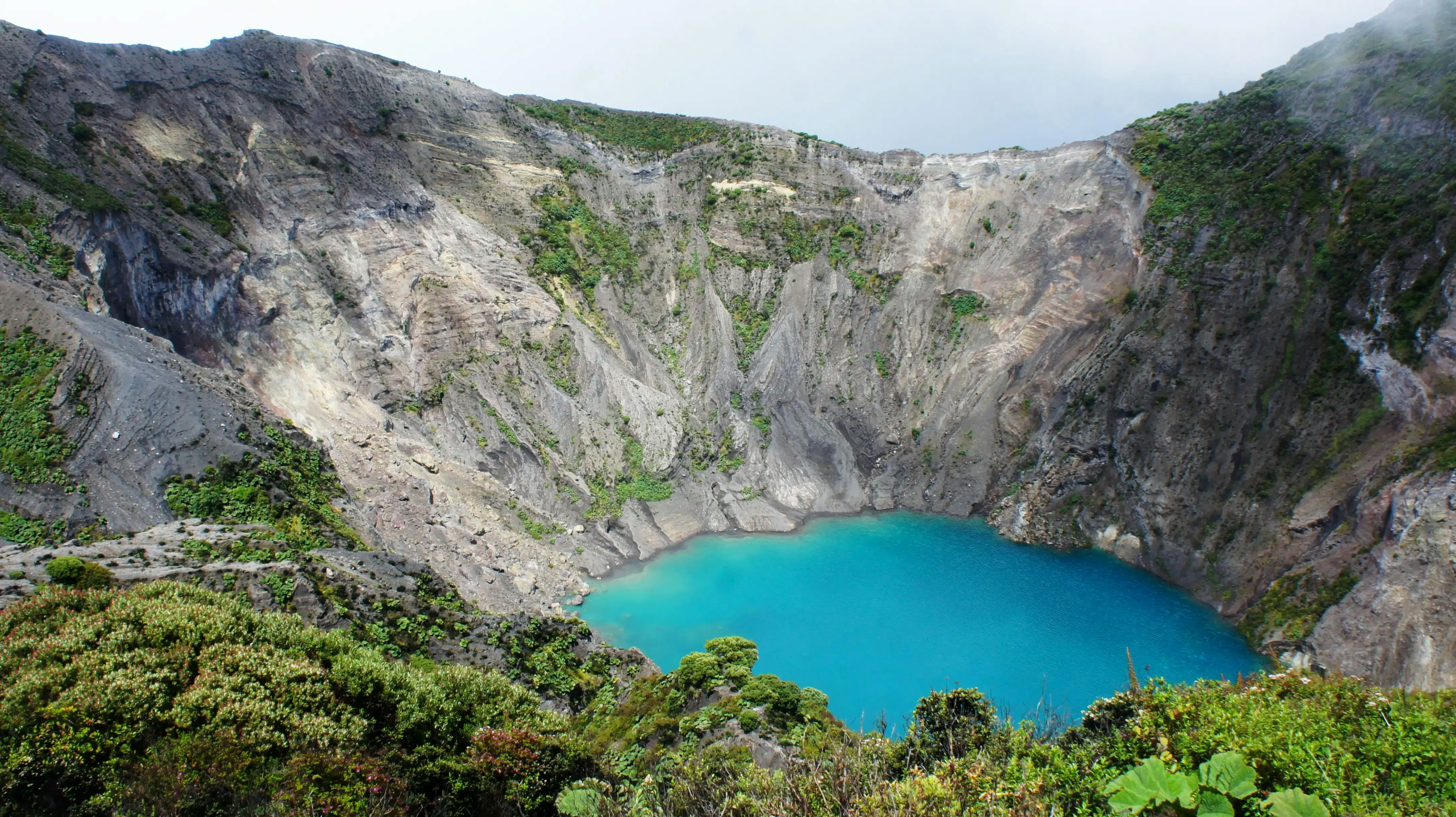 Laguna vulcanica circondata da montagne e vegetazione in un paesaggio naturale mozzafiato